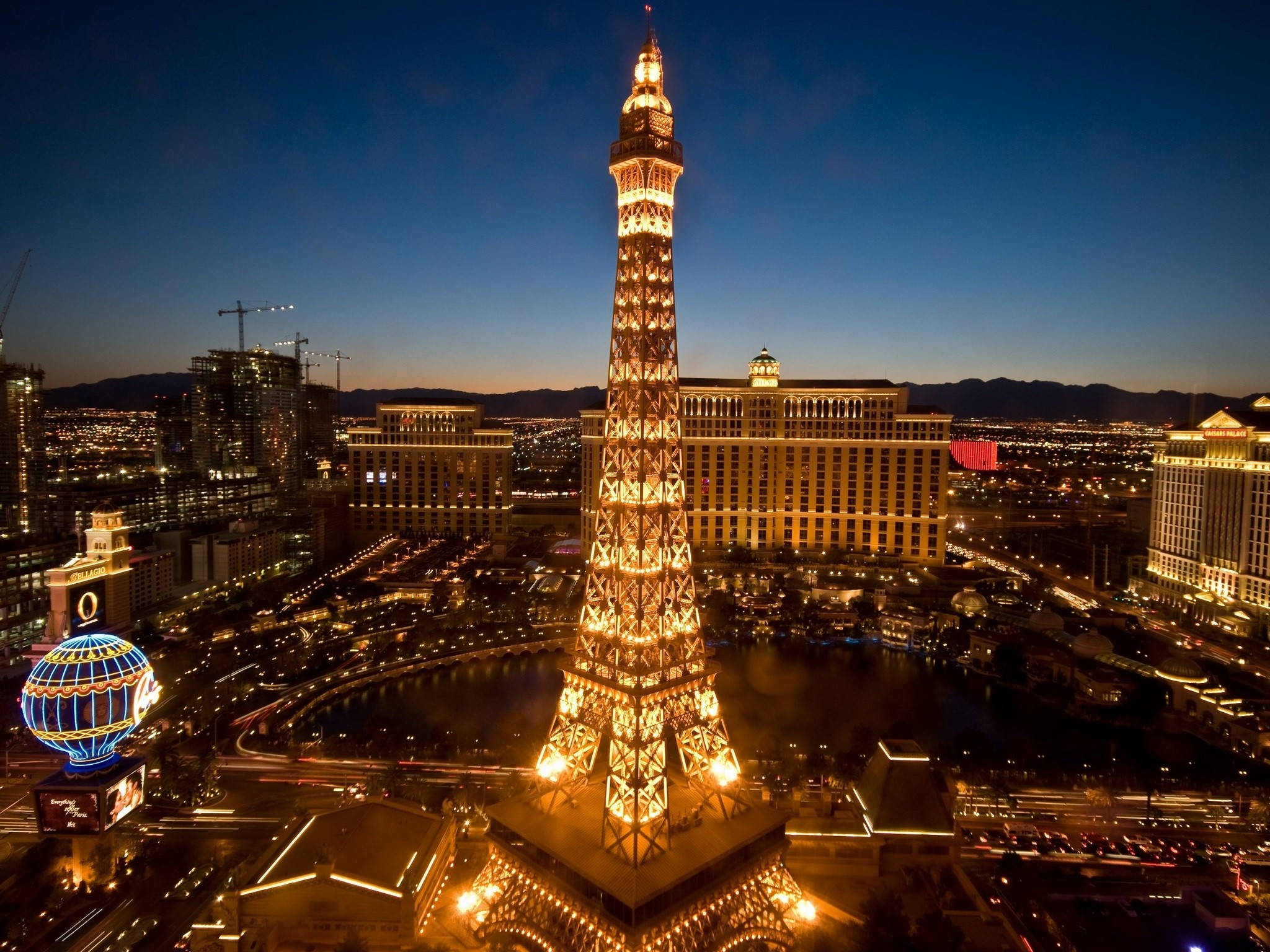 Las Vegas 桌布 壁紙 — 拉斯維加斯黃昏的天空下，一座耀眼的艾菲爾鐵塔複製品溫暖地發光，周圍是燈火通明的酒店和繁華的城市燈光。