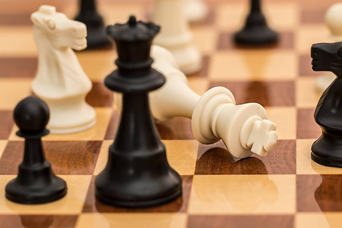 西洋棋 桌布 壁紙 — 拋光木方格上棋盤的特寫，顯示倒下的白王和站立的黑棋。