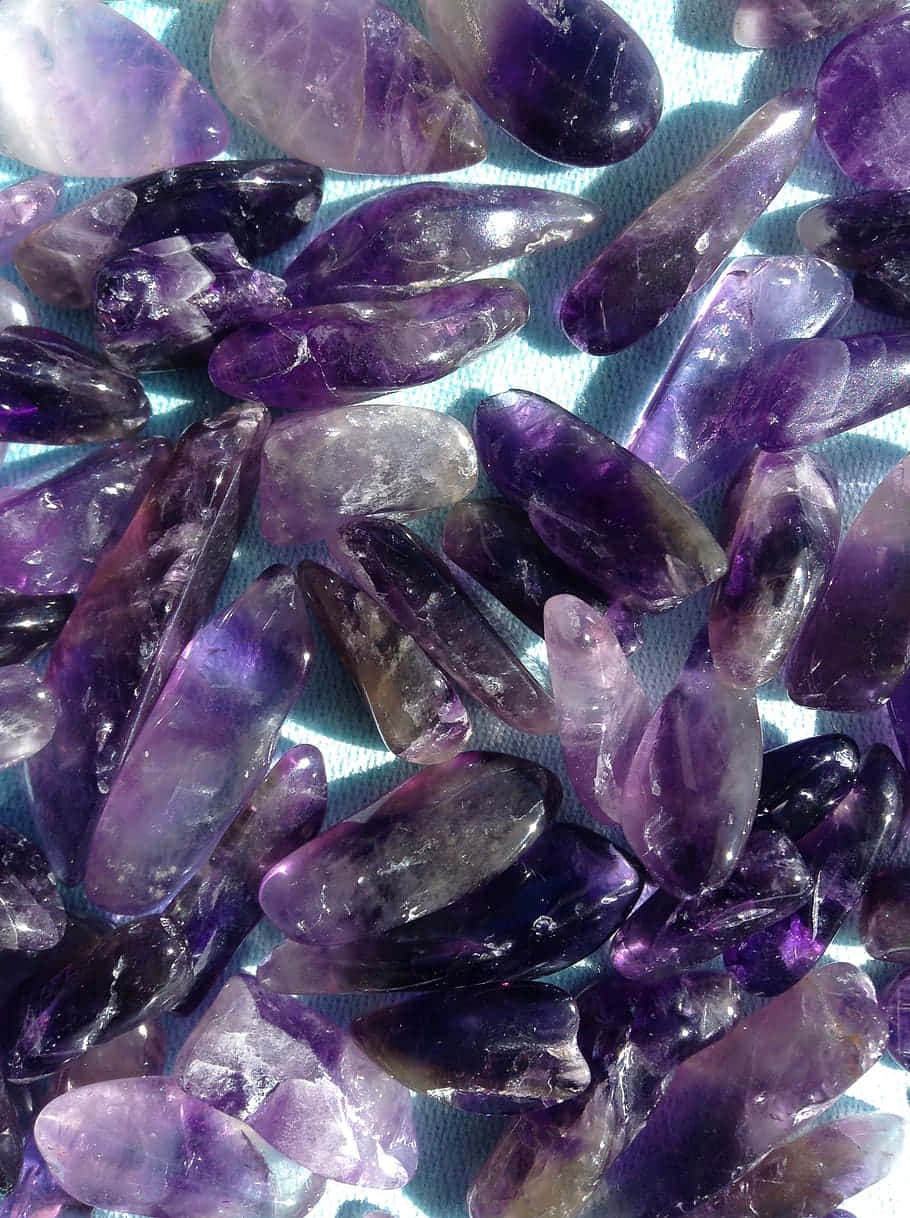 紫水晶 桌布 壁紙 — 拋光紫水晶晶體的近距離特寫，呈現不同深淺的紫色，放置在淺藍色紋理表面上。