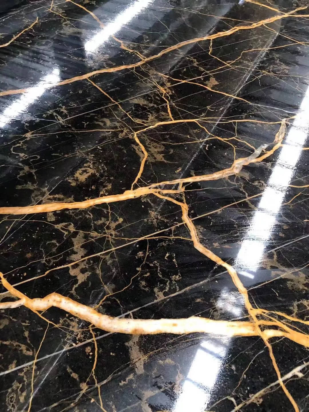 大理石 桌布 壁紙 — 拋光黑色大理石地板，帶有複雜的金色紋理，反射明亮的天花板燈光。