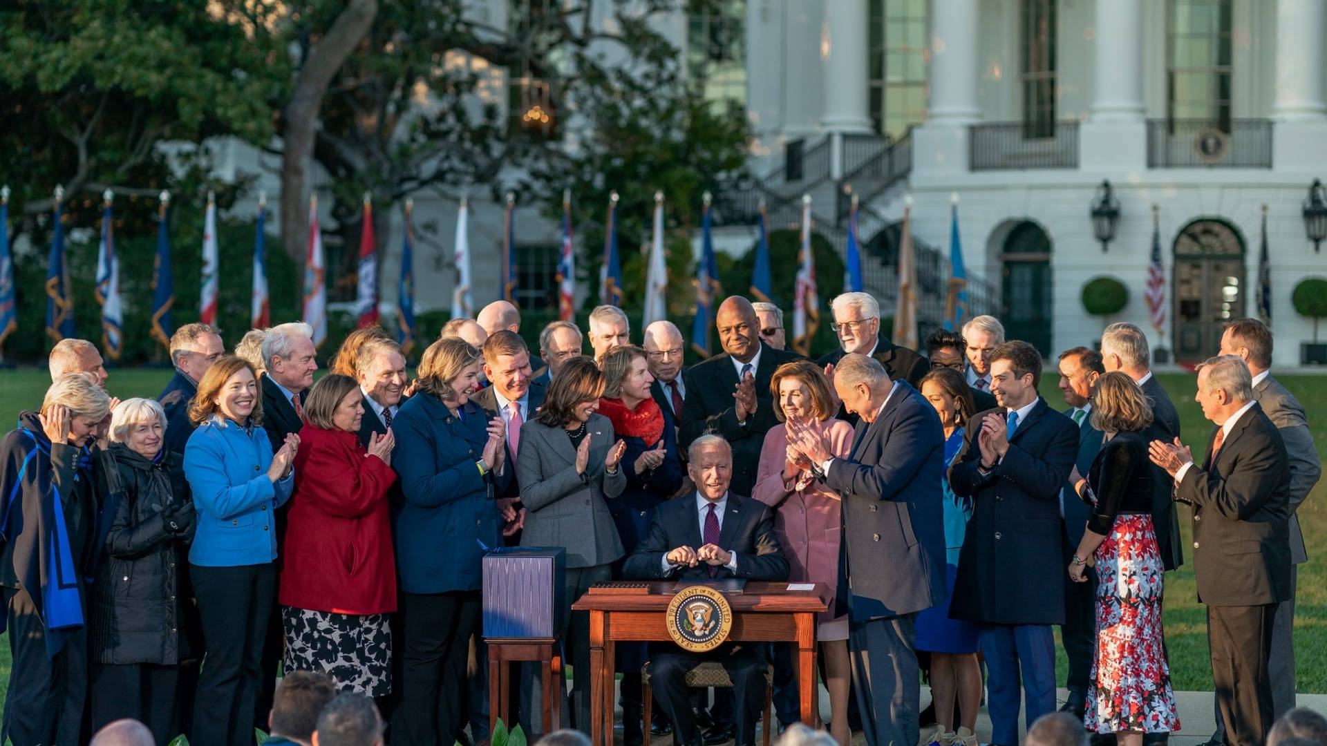 Nancy Pelosi 桌布 壁紙 — 拜登總統在白宮簽署行政命令，前景有官員鼓掌，背後有旗幟。