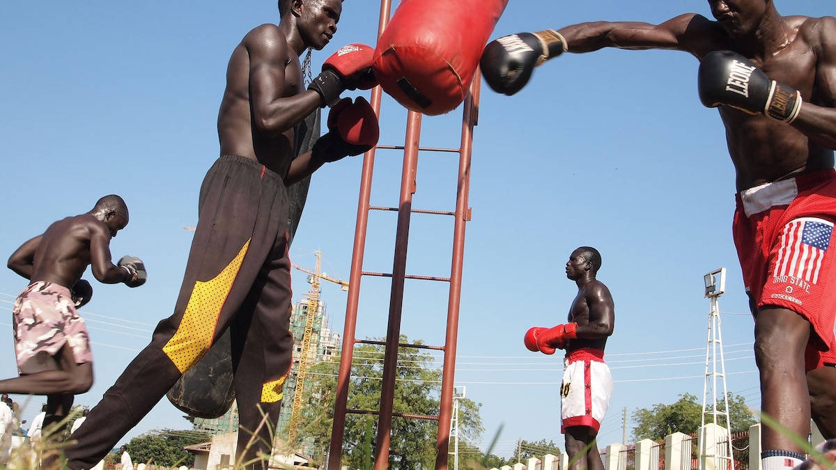 South Sudan 桌布 壁紙 — 拳擊手在明亮的陽光下戶外訓練，背景有紅色沙包和建築起重機。
