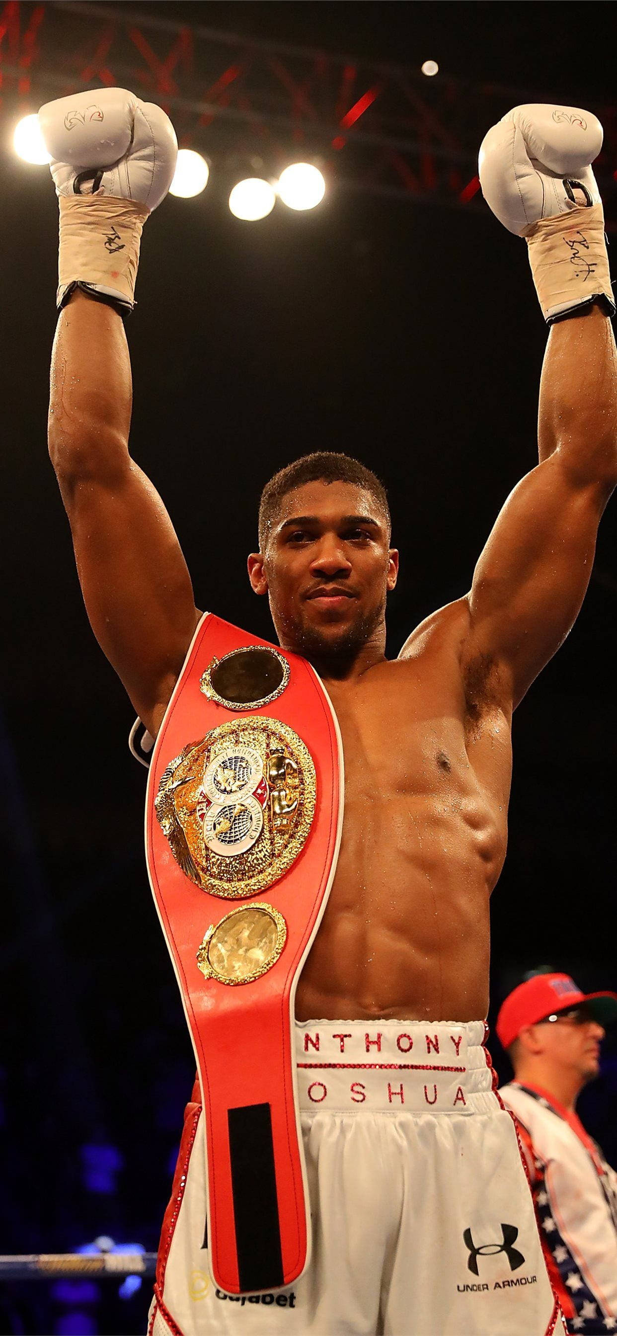 Anthony Joshua 桌布 壁紙 — 拳擊手安東尼·約書亞在明亮的場館燈光下，勝利地高舉雙臂，手持冠軍腰帶。