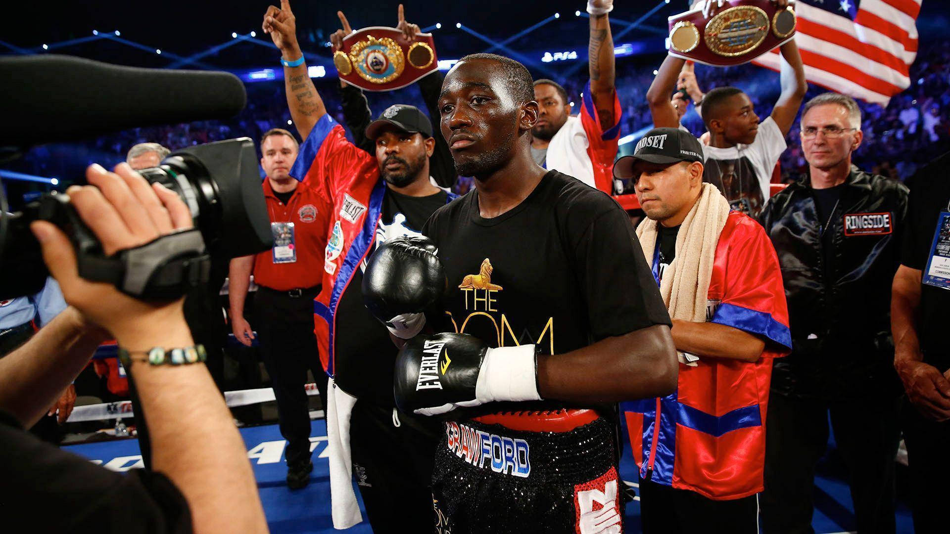 Champion 桌布 壁紙 — 拳擊手特倫斯·克勞福德在擂台上勝利地站著，手持冠軍腰帶，他的團隊在明亮的場館燈光下圍繞他慶祝。