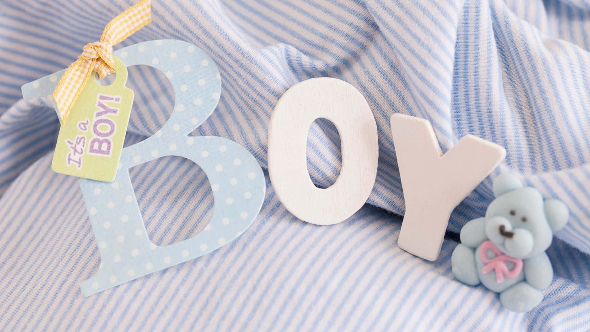 男孩 桌布 壁紙 — 拼出「BOY」的木製字母放在條紋布上面，旁邊有一隻泰迪熊和一個寫著「It's a BOY!」的標籤