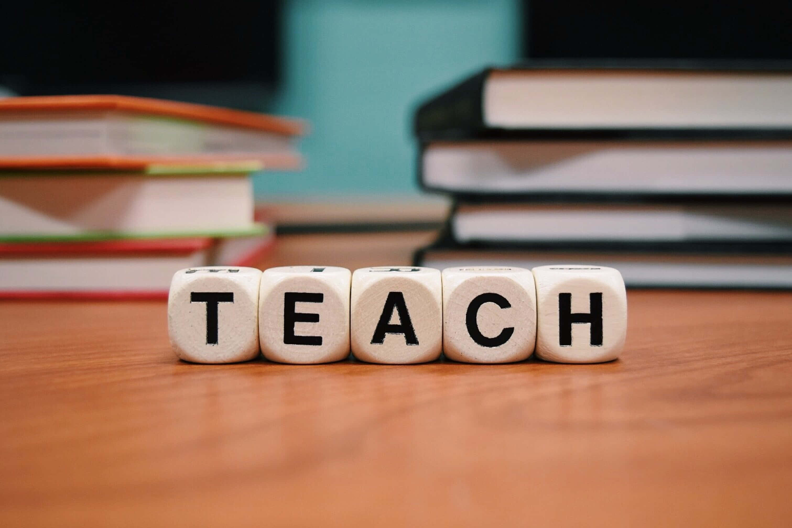 Dice 桌布 壁紙 — 拼出 TEACH 的木製積木放在一張被書堆包圍的書桌上，營造專注的學習環境。