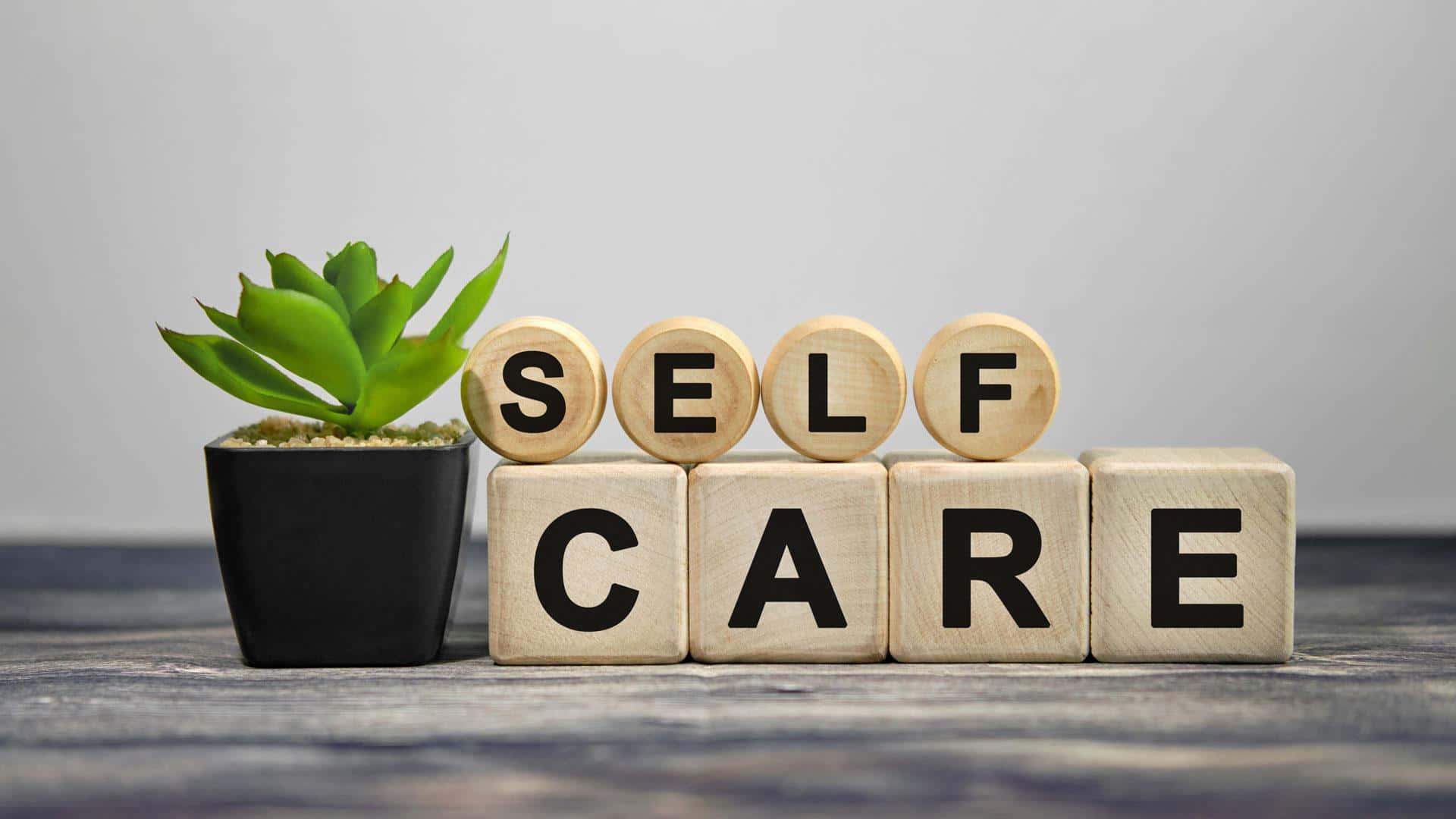 Self Care 桌布 壁紙 — 拼出「自我照顧」的木塊放在一個質樸的木質表面上，旁邊有一盆多肉植物。