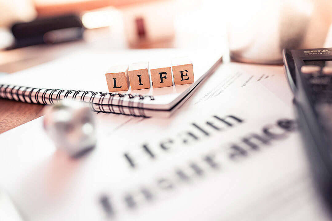 life 桌布 壁紙 — 拼出LIFE的木塊放在螺旋筆記本上，筆記本下方是健康保險文件，附近有計算機。