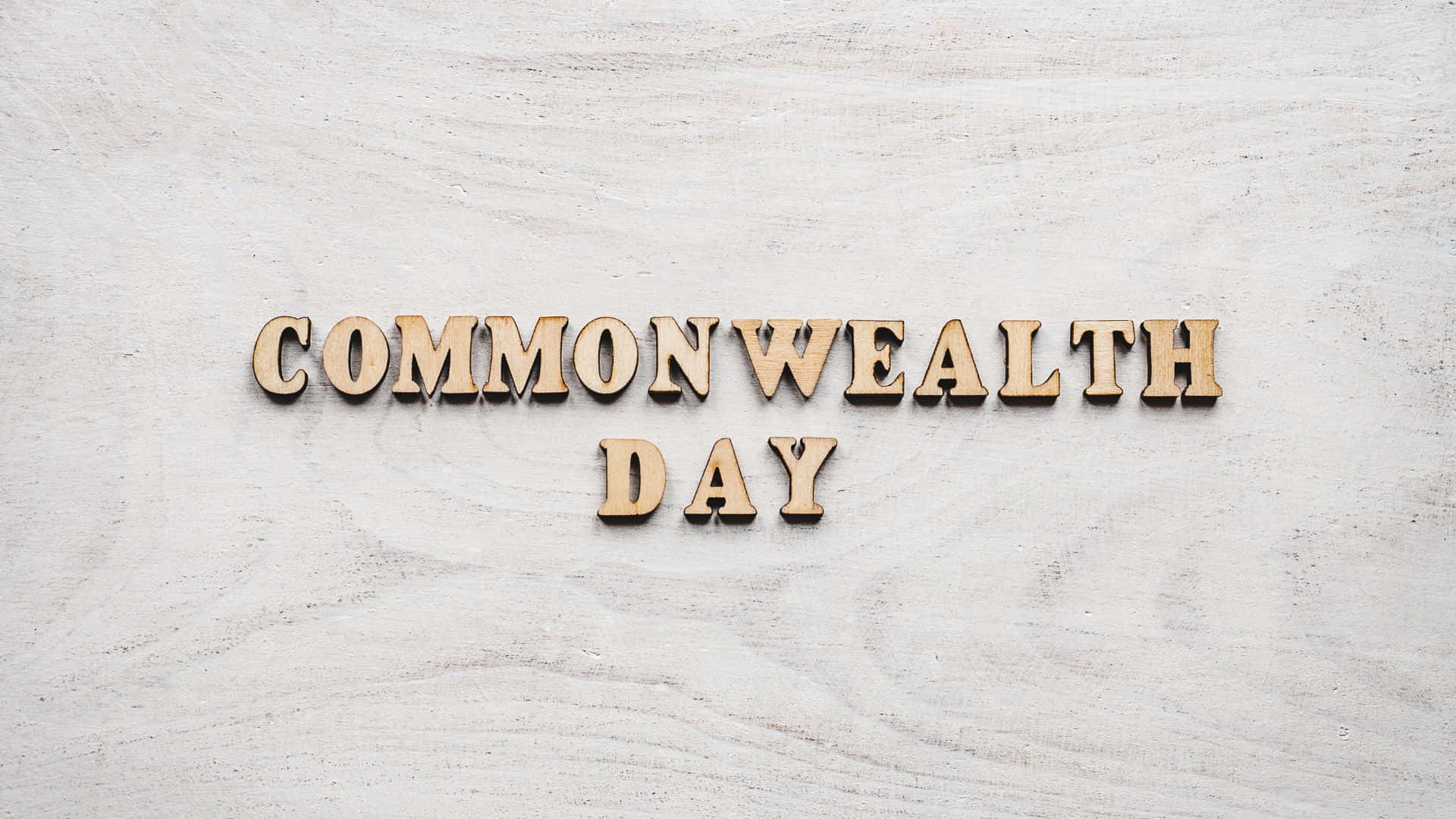 Commonwealth Day 桌布 壁紙 — 拼寫 COMMONWEALTH DAY 的木製字母放置在淺色紋理表面上，構成極簡主義構圖。