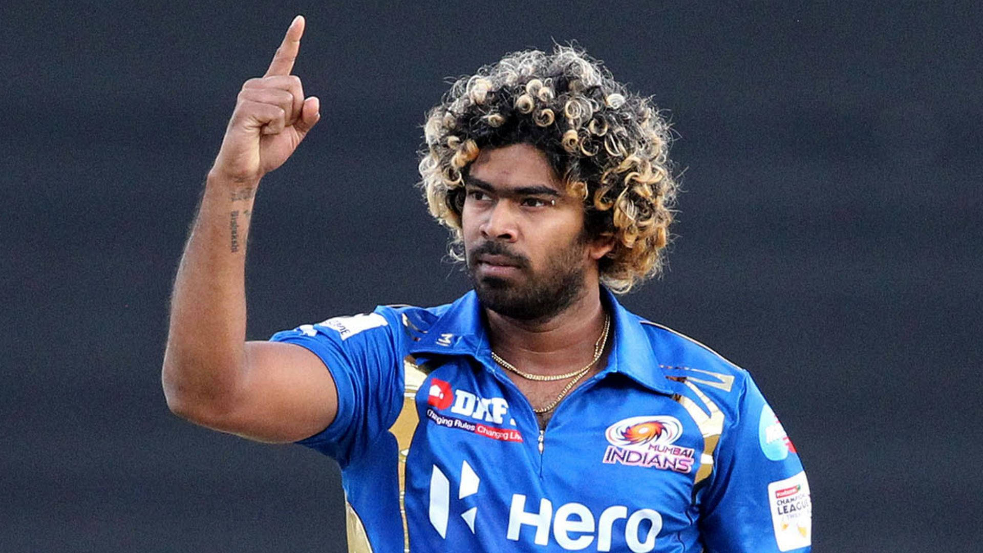Sri Lanka Cricket 桌布 壁紙 — 捲髮的板球運動員在深色背景下穿著藍色Mumbai Indians球衣向上指。