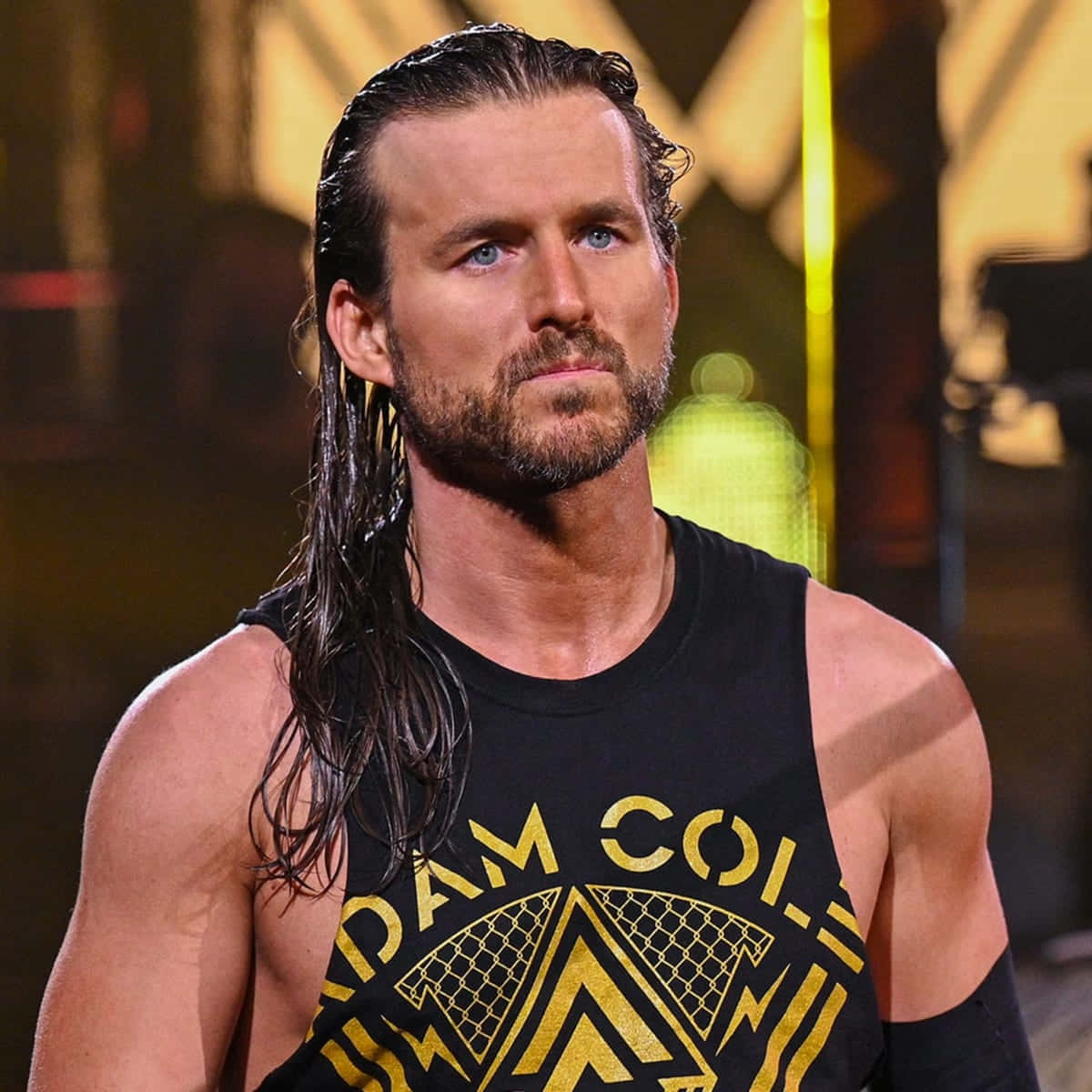 professional 桌布 壁紙 — 摔角手 Adam Cole 濕髮留鬍，在燈光璀璨的競技場中穿著黑色金色背心，凝視前方。