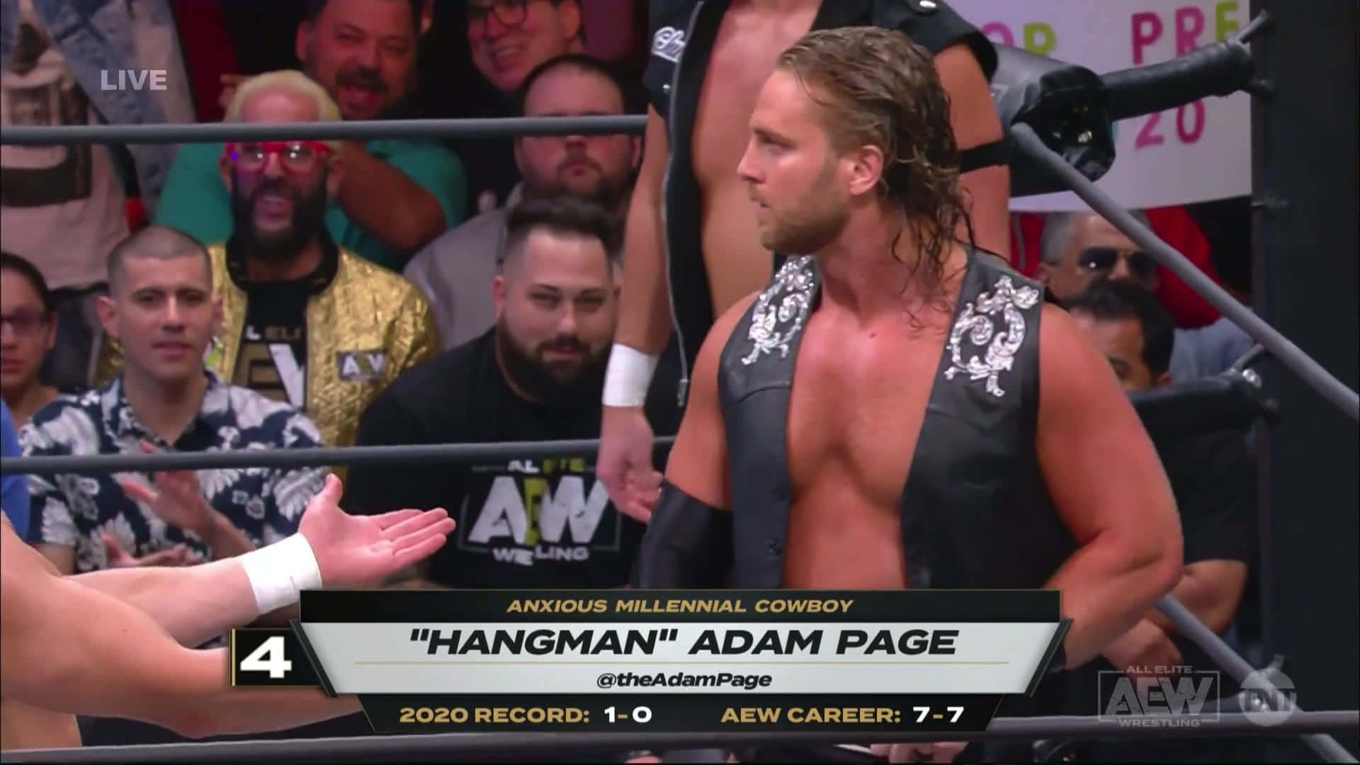 摔角 桌布 壁紙 — 摔角手 Adam Page 身穿黑色背心站在擂台上，觀眾在 AEW 比賽期間專注觀看。