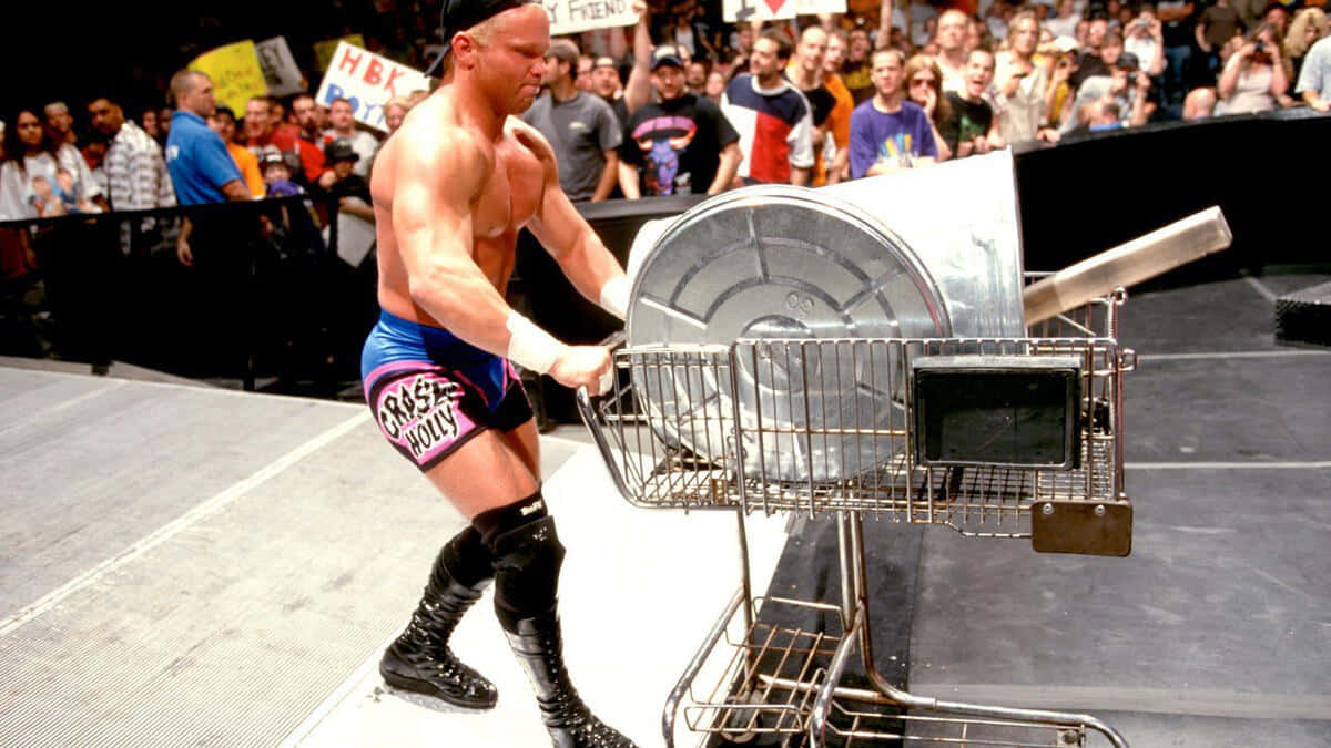 Crash Holly 桌布 壁紙 — 摔角手 Chris Jericho 在明亮的場館燈光下，推著裝有大型金屬桶的購物車穿過摔角擂台。