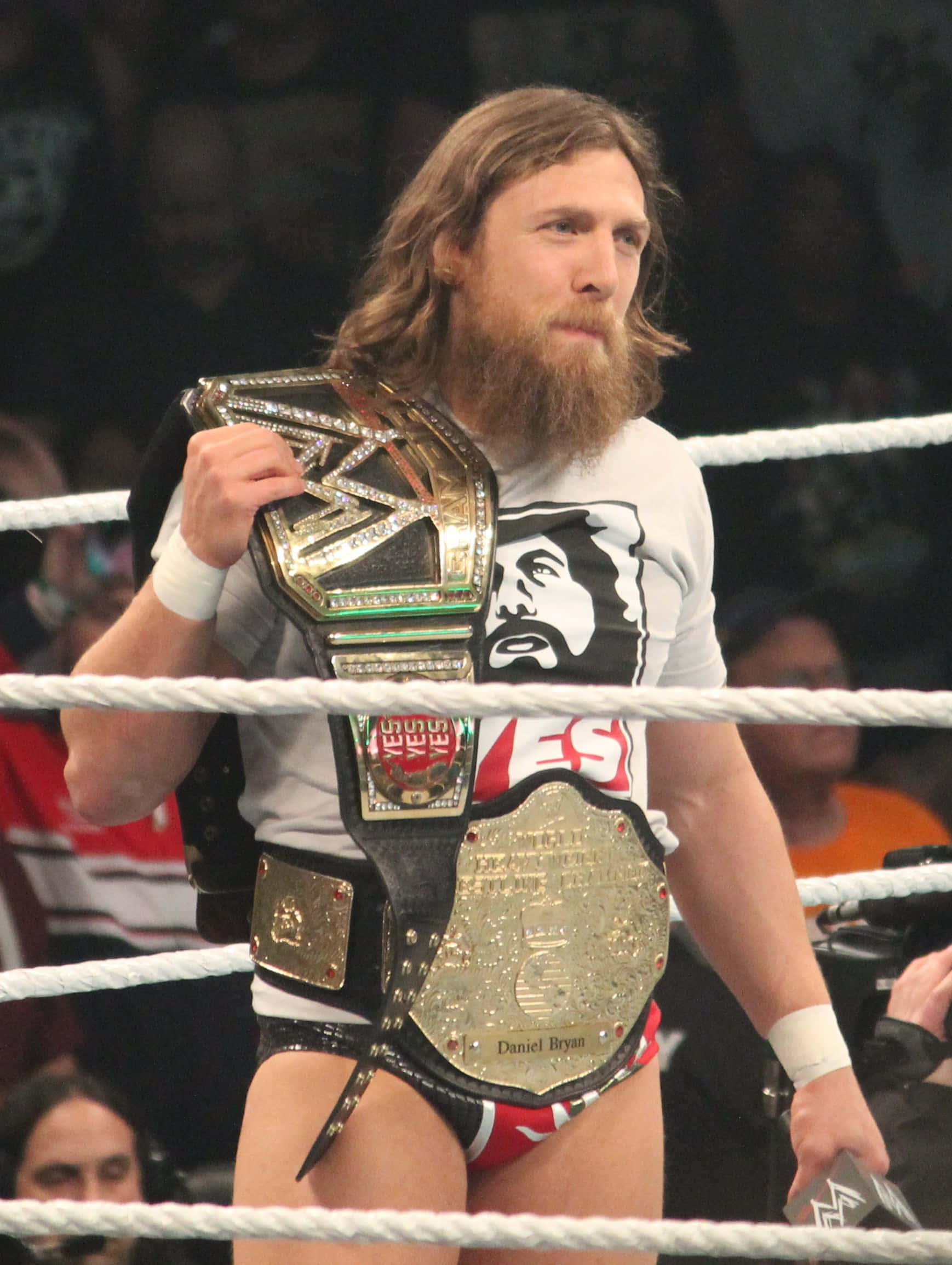 摔角 桌布 壁紙 — 摔角手 Daniel Bryan 站在擂台上，手持多條冠軍腰帶，神情專注。