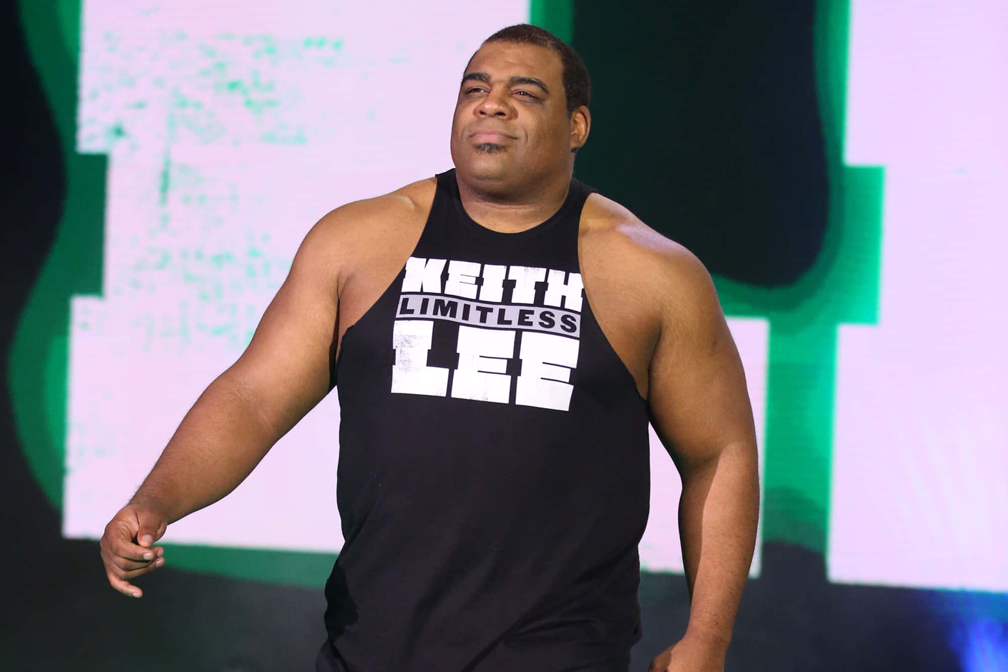 Aew 桌布 壁紙 — 摔角手 Keith Lee 身穿印有白色文字的黑色背心，在明亮燈光下自信地站在舞台上。