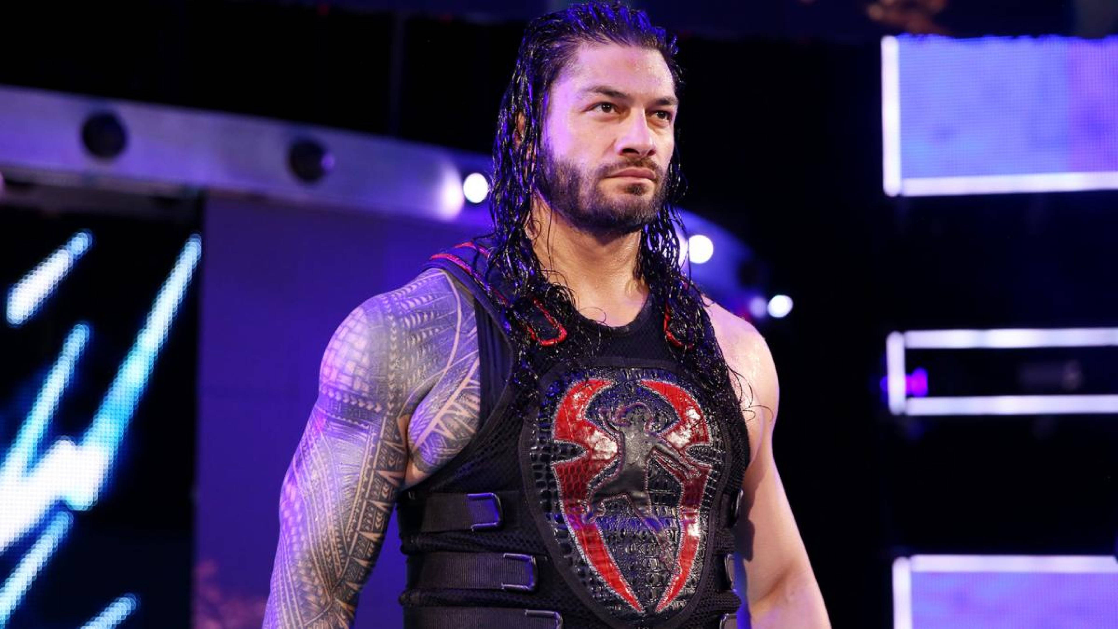 Roman 桌布 壁紙 — 摔角手 Roman Reigns 自信地站在紫色舞台燈光下，身穿帶有紅色蜘蛛標誌的黑色背心。