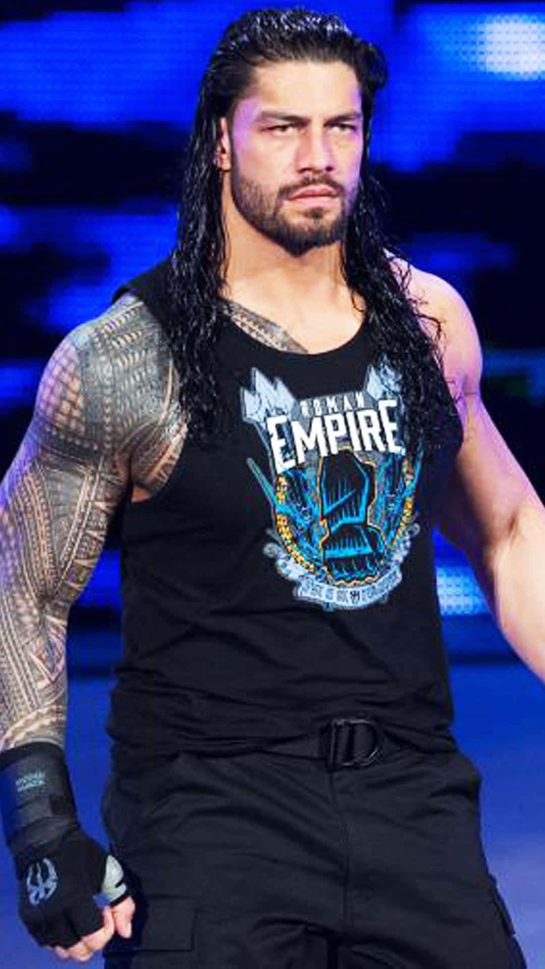 Roman Reigns 桌布 壁紙 — 摔角手 Roman Reigns 留著長黑髮和刺青，在藍色舞台燈光下穿著黑色背心，眼神銳利。