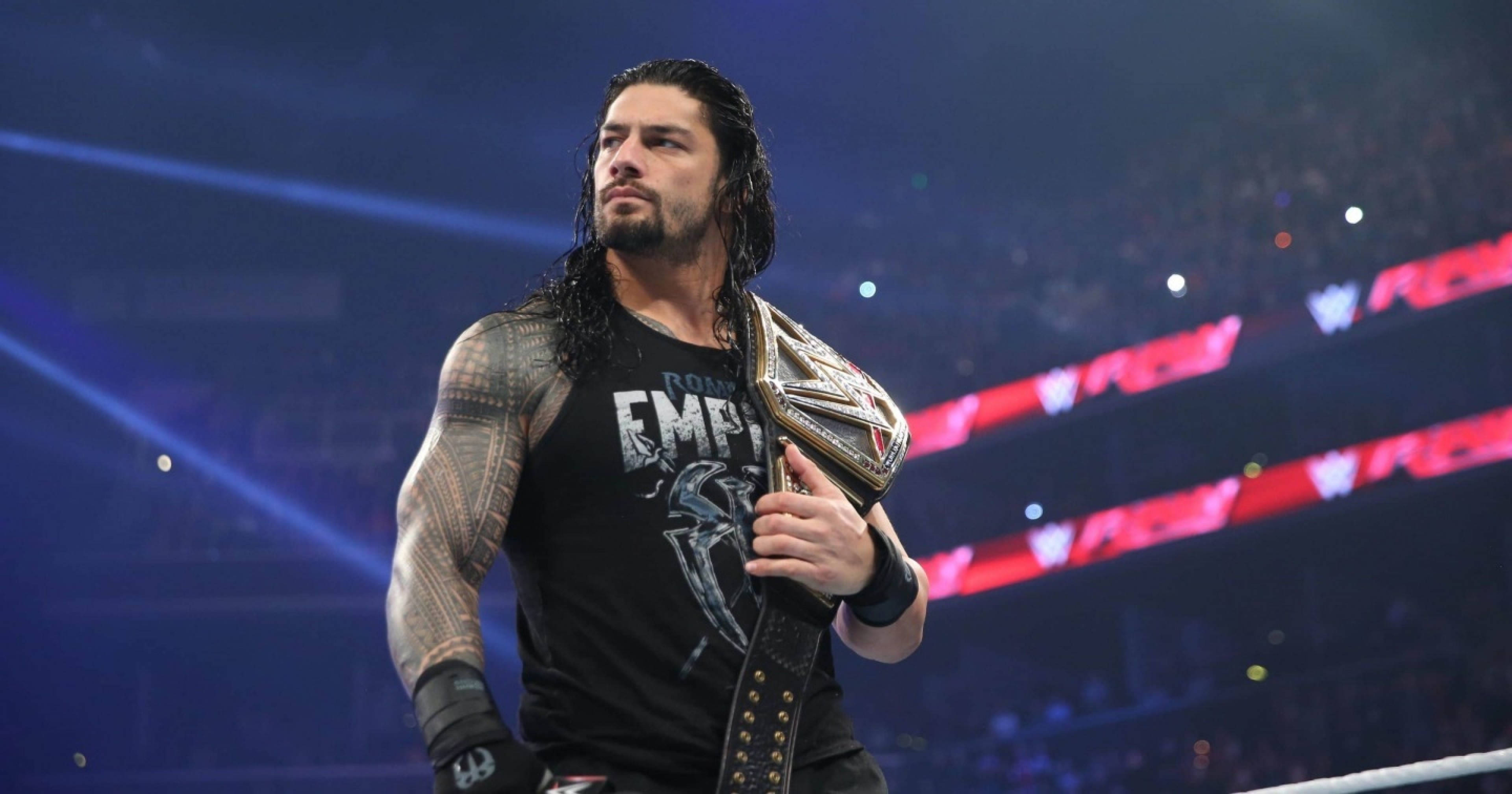 Roman 桌布 壁紙 — 摔角手 Roman Reigns 站在擂台上，在明亮的場館燈光下手持冠軍腰帶，背景有觀眾。