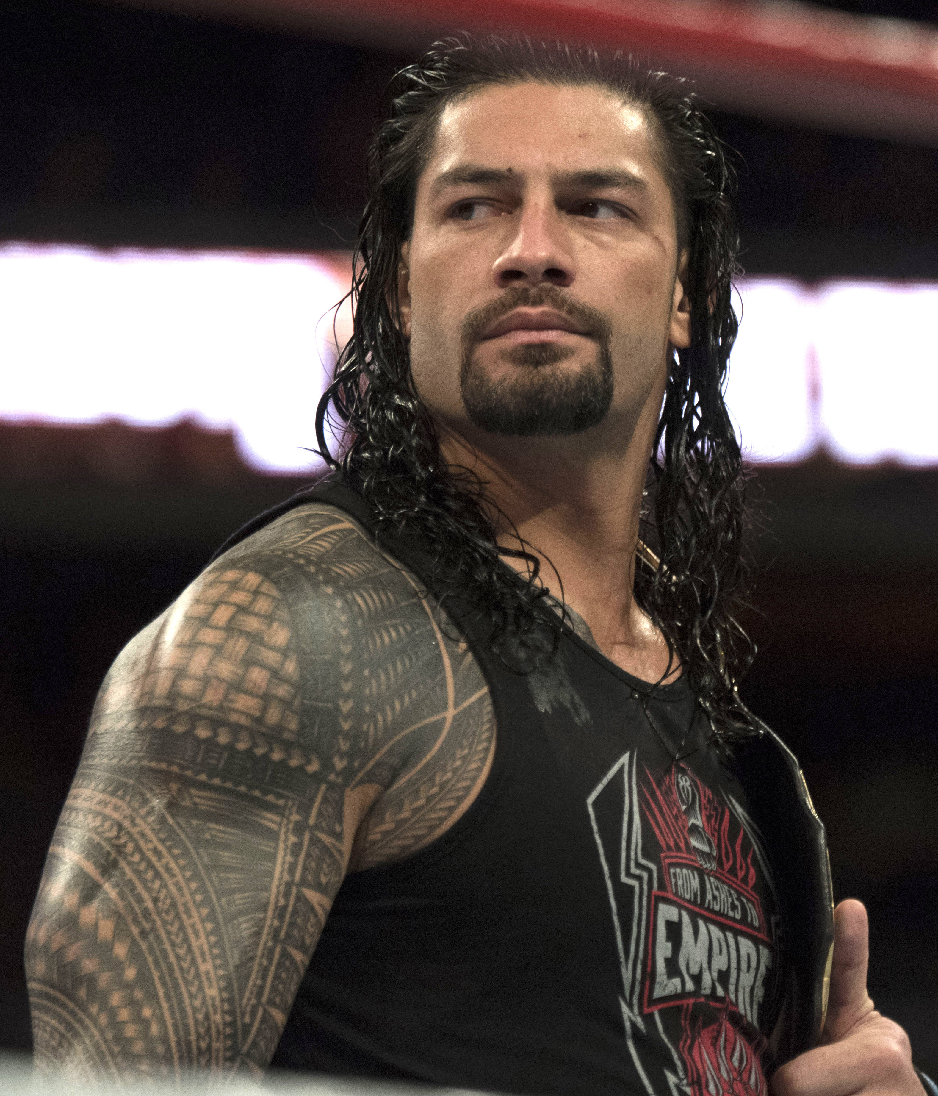 Roman 桌布 壁紙 — 摔角手 Roman Reigns 留著長黑髮，手臂上有複雜的紋身，在明亮的場館燈光下於擂台上專注地凝視。