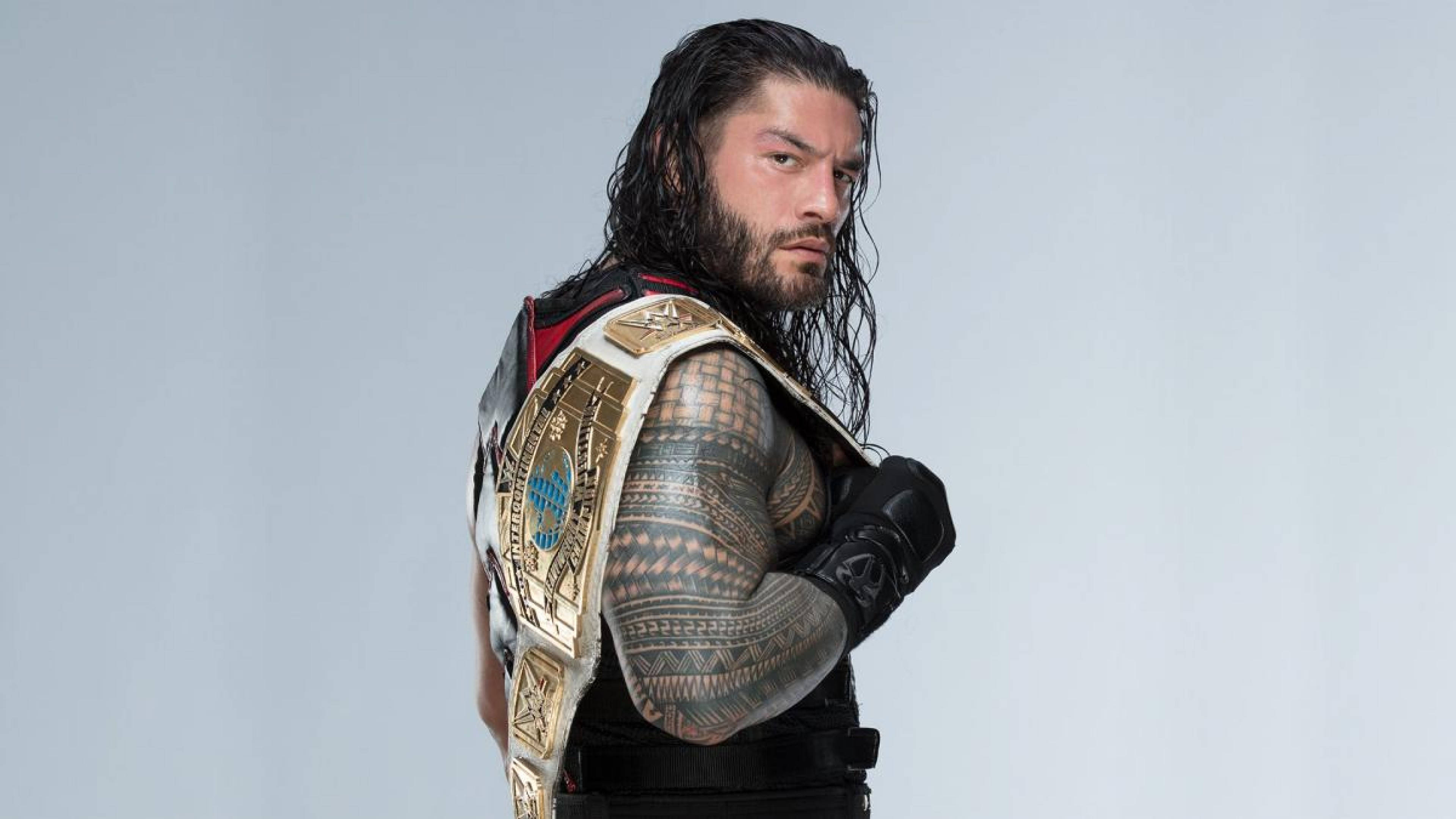 Roman 桌布 壁紙 — 摔角手 Roman Reigns 將冠軍腰帶搭在肩上，在純灰色背景前凝視著。