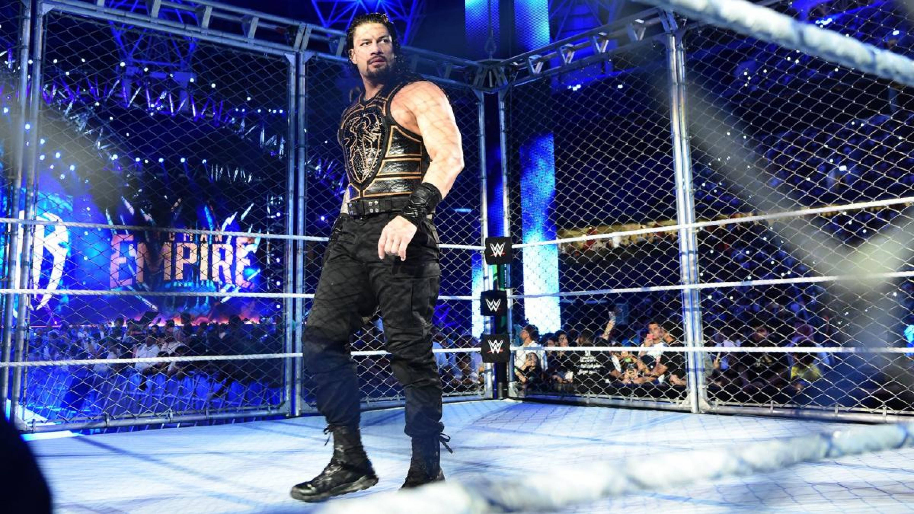Roman 桌布 壁紙 — 摔角手 Roman Reigns 在明亮的藍色場館燈光下，於鋼鐵籠擂台內霸氣站立，圍欄後有歡呼的粉絲。