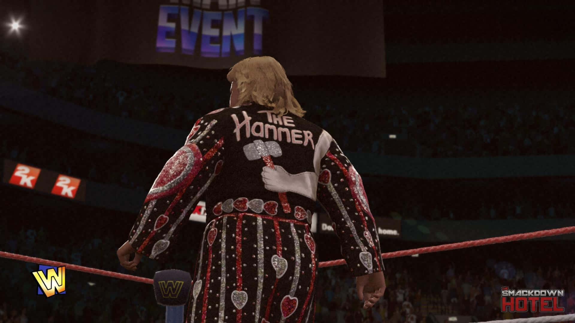 WWE 桌布 壁紙 — 摔角手 The Hammer 站在摔角場上，身穿帶有紅色心形和銀色裝飾的黑色外套，在場館燈光下面向人群。