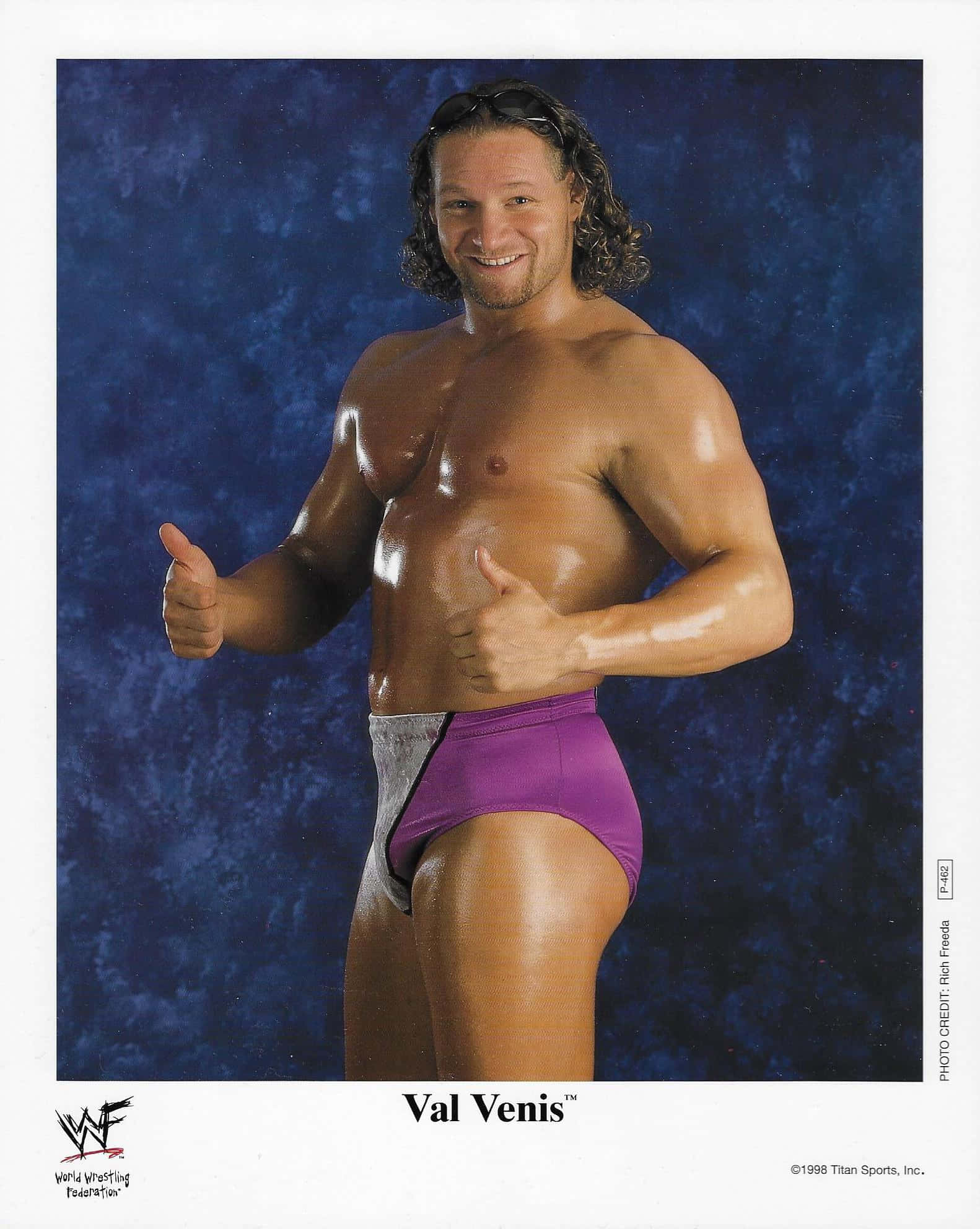 Canadian 桌布 壁紙 — 摔角手 Val Venis 自信地穿著紫色短褲，在帶有紋理的藍色背景前豎起雙拇指。