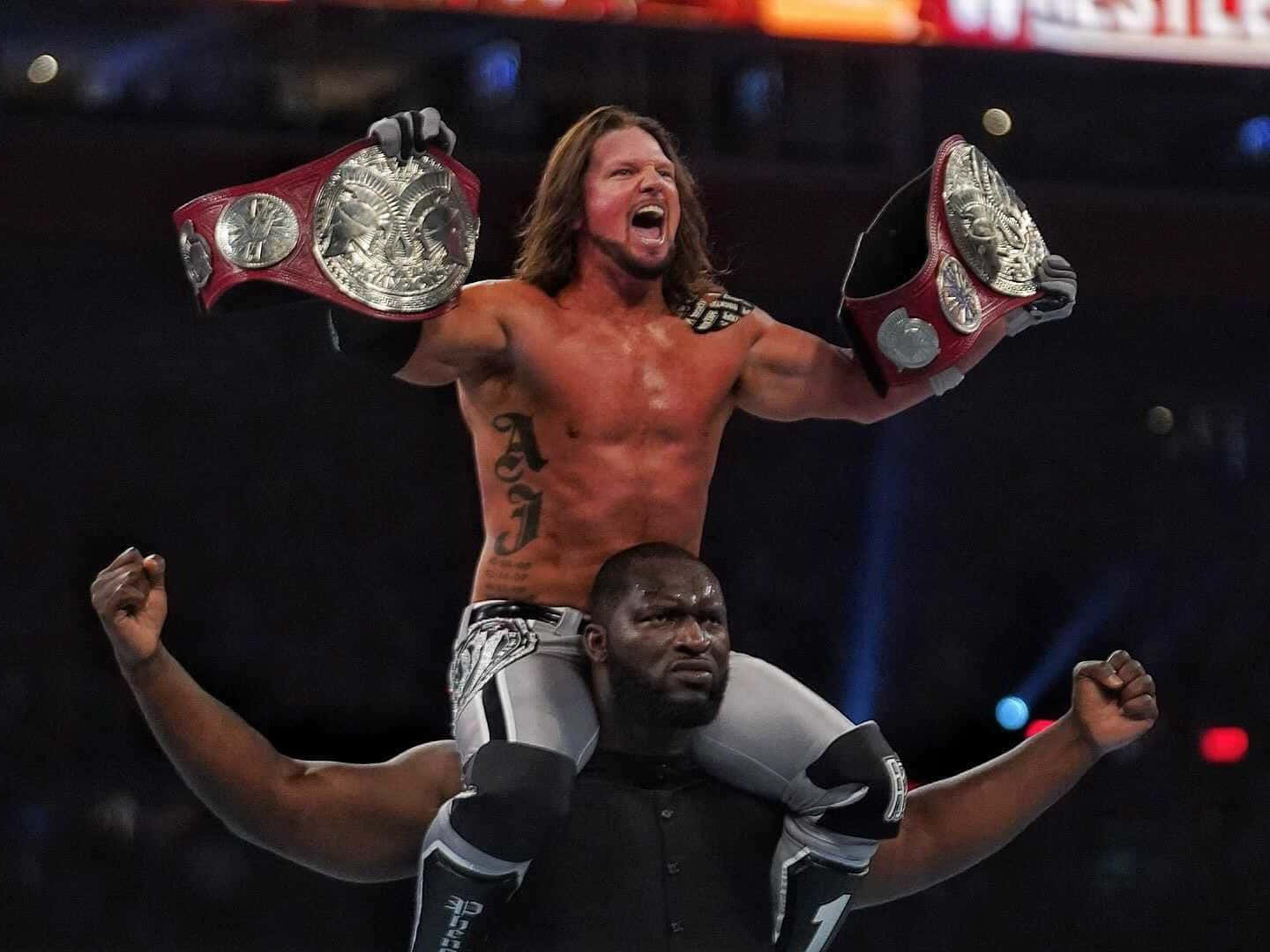 WWE 桌布 壁紙 — 摔角手AJ Styles在燈光明亮的場館中，站在搭檔的肩膀上，高舉兩條冠軍腰帶，勝利姿態盡顯。