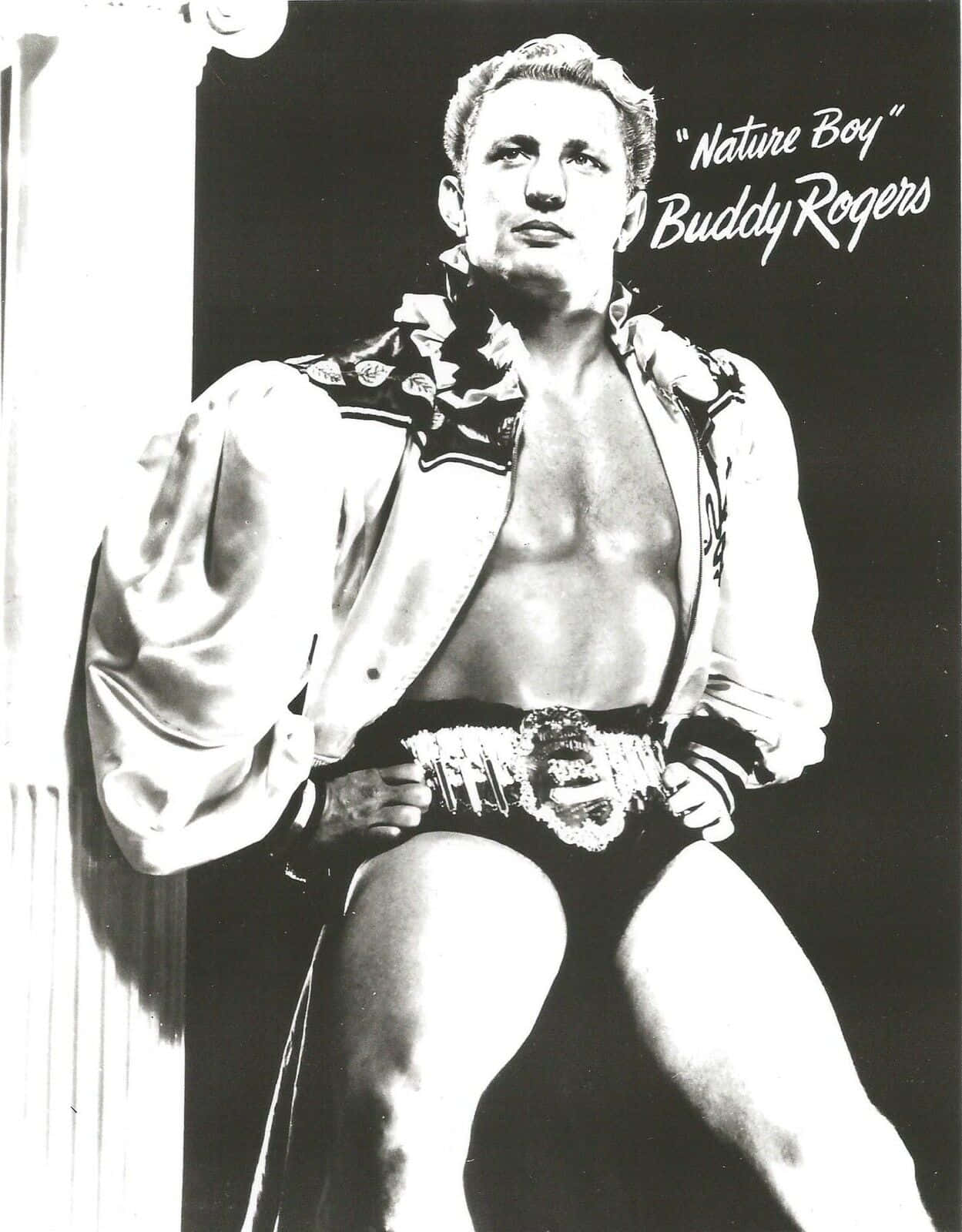 WWE 桌布 壁紙 — 摔角手Buddy Rogers的黑白肖像，自信地擺姿勢，帶著冠軍腰帶和敞開的夾克，背景黑暗。