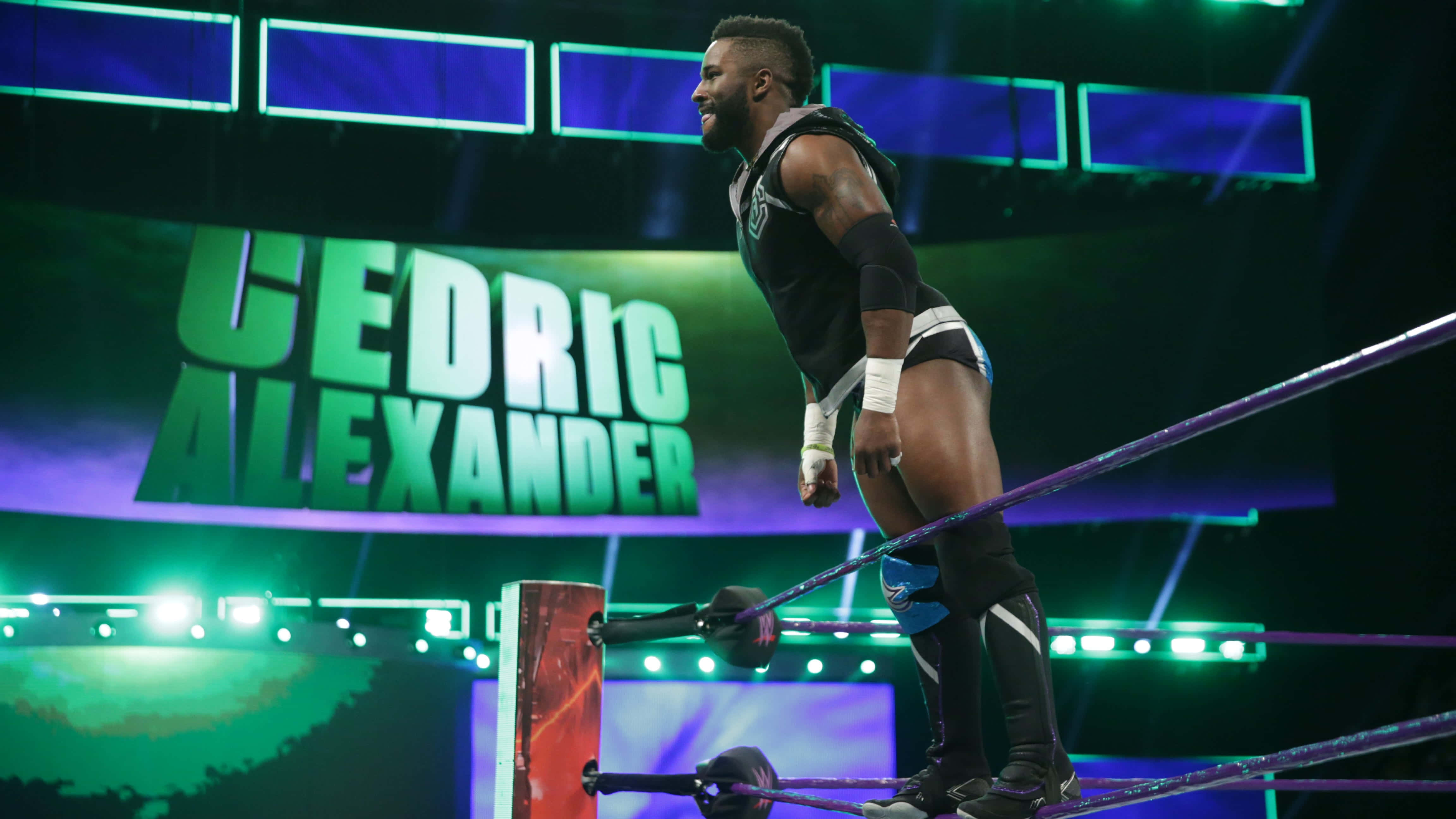 WWE 桌布 壁紙 — 摔角手Cedric Alexander站在燈光明亮的擂台上，頂繩上，在充滿活力的綠色和藍色舞台燈光下。