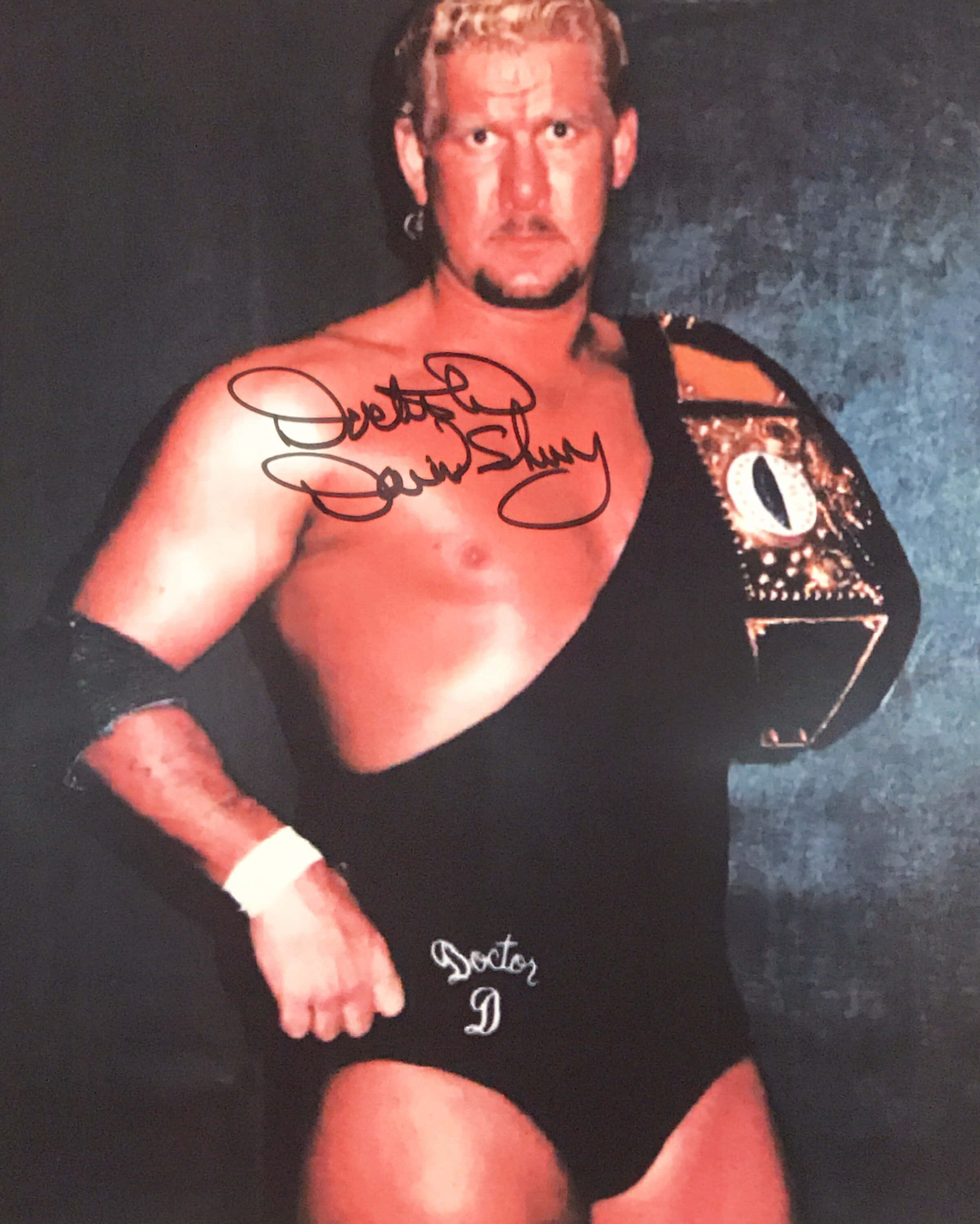 WWE 桌布 壁紙 — 摔角手Doctor X自信地擺姿勢，身穿黑色緊身衣，冠軍腰帶搭在肩上，背景為深色紋理。