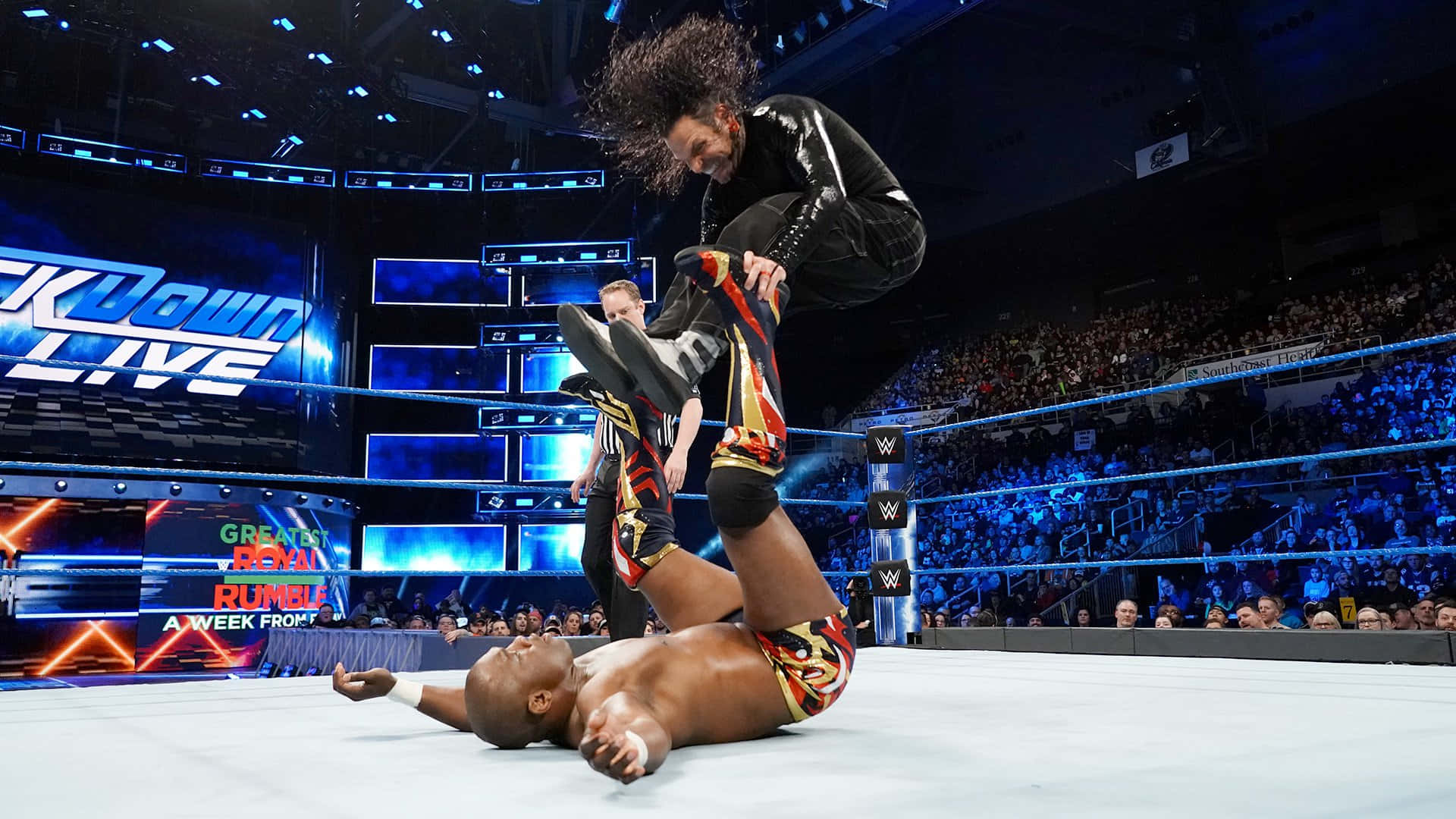 WWE 桌布 壁紙 — 摔角手在明亮的場館燈光下跳過對手，背後是咆哮的人群。