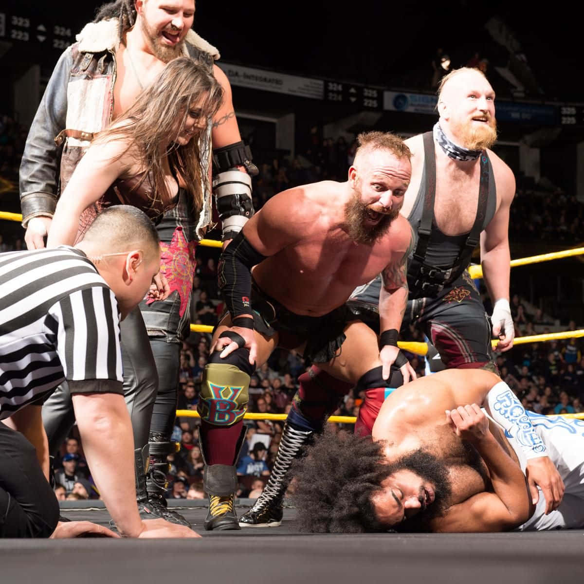 Wrestling 桌布 壁紙 — 摔角手在混亂的擂台鬥毆中，裁判在一旁觀看，一名摔角手在明亮的場館燈光下壓制另一名摔角手。