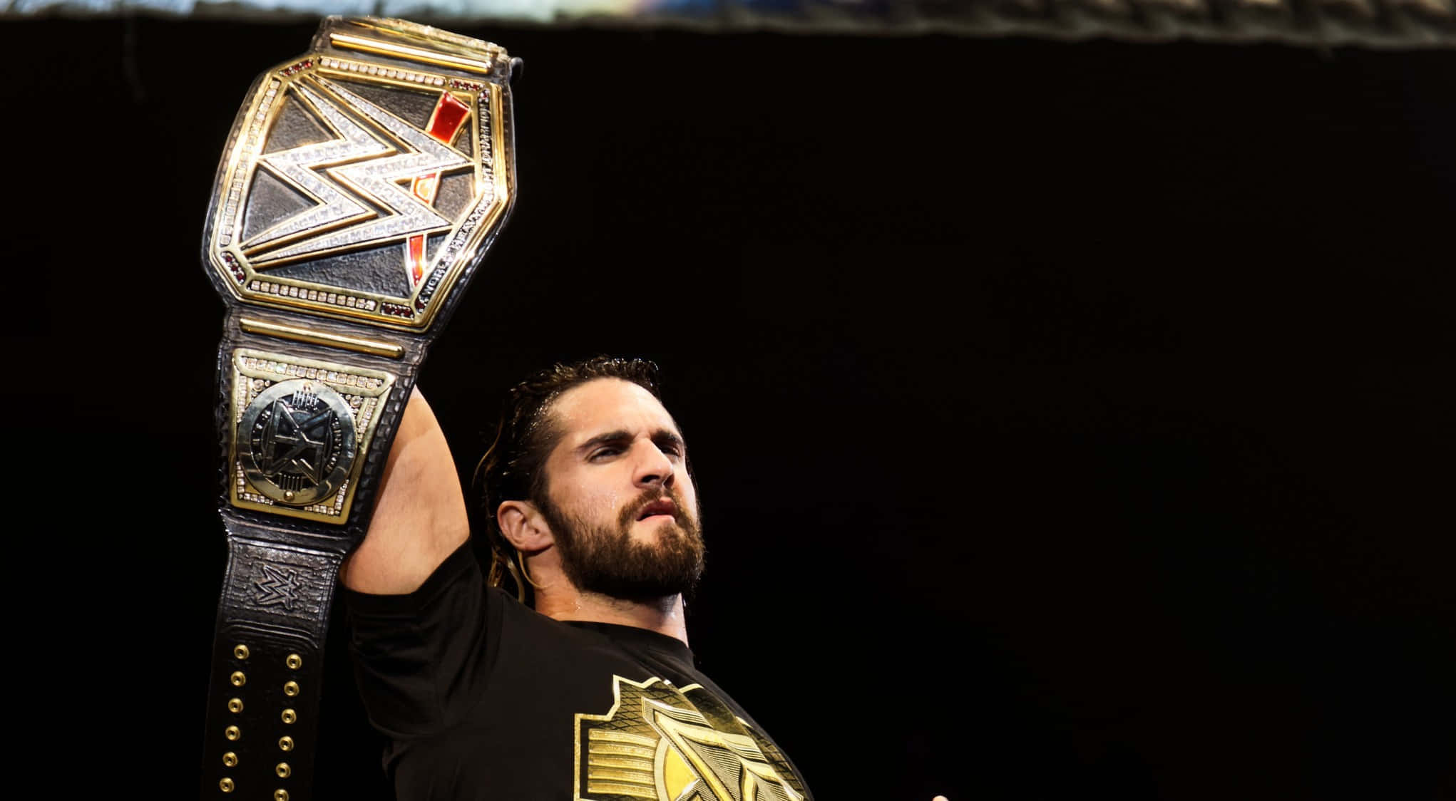 WWE 桌布 壁紙 — 摔角手在黑暗舞台背景下，勝利地舉起閃亮的WWE冠軍腰帶。