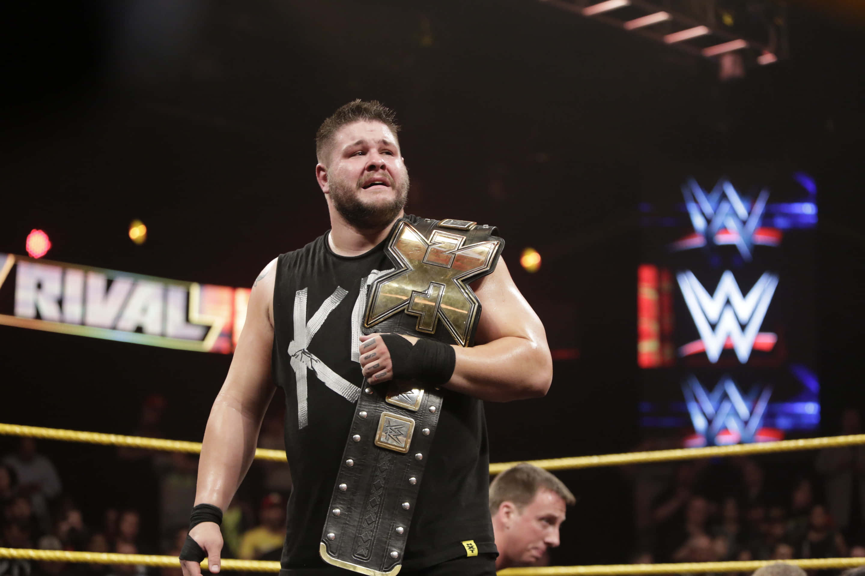 WWE 桌布 壁紙 — 摔角手帶著冠軍腰帶，在明亮的場館燈光下於擂台上勝利地站立。