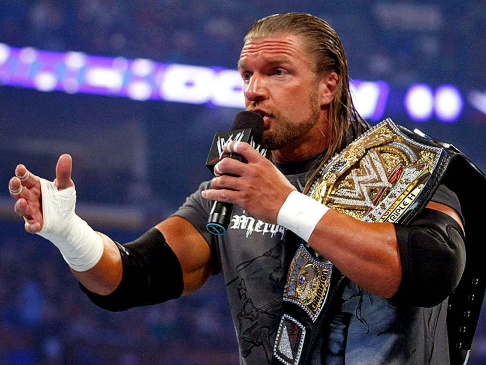 WWE 桌布 壁紙 — 摔角手帶著冠軍腰帶和麥克風，在明亮的燈光下向競技場的觀眾講話。