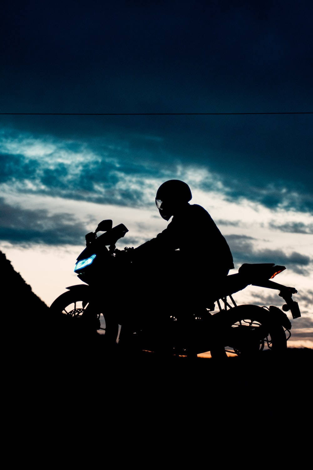 Silhouette 桌布 壁紙 — 摩托車手在摩托車上的剪影，背景是戲劇性的暮色天空，車頭燈發出光芒。