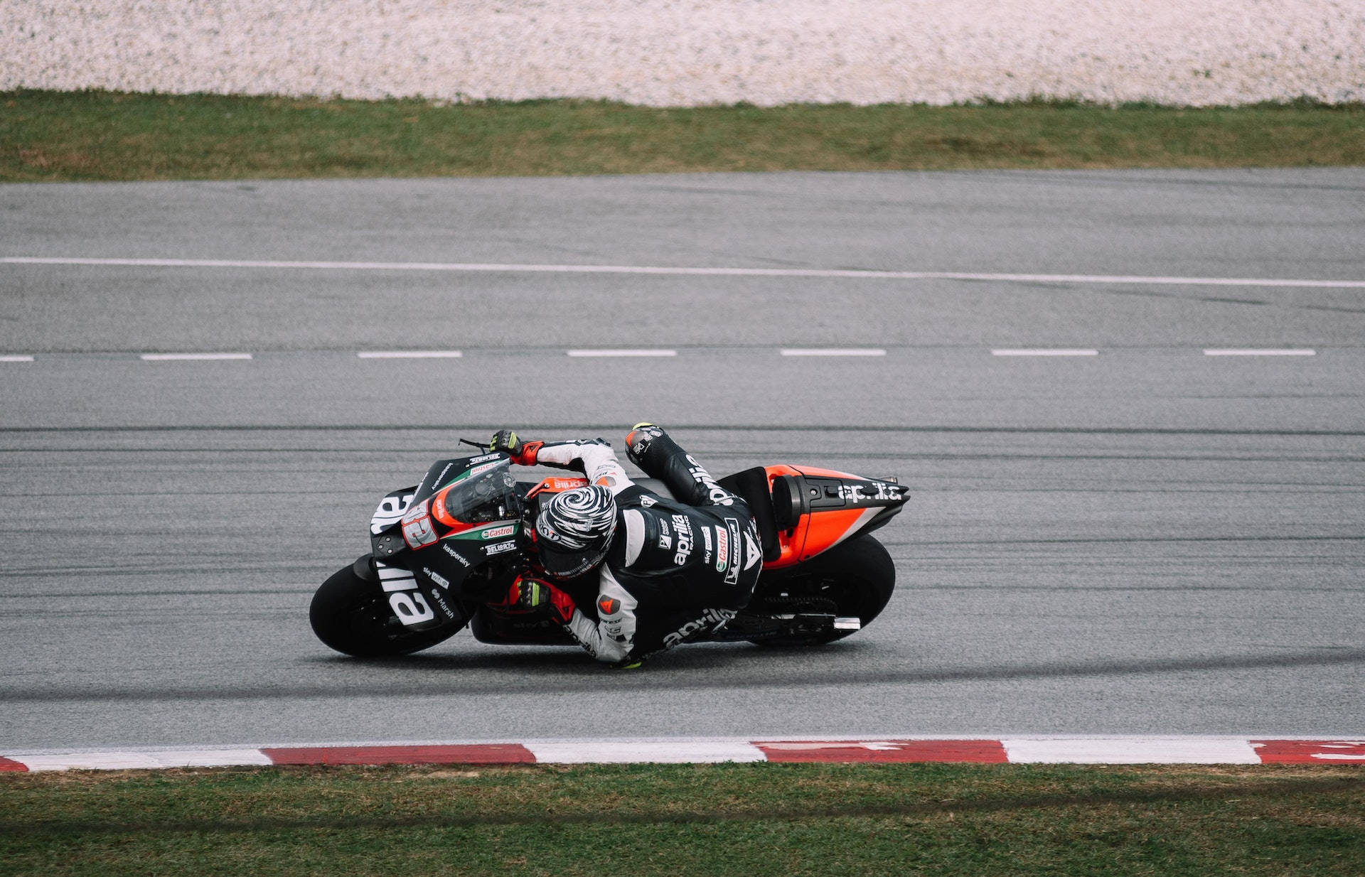 Racing 桌布 壁紙 — 摩托車手在賽道上急彎，賽道有紅白路緣石和碎石緩衝區。