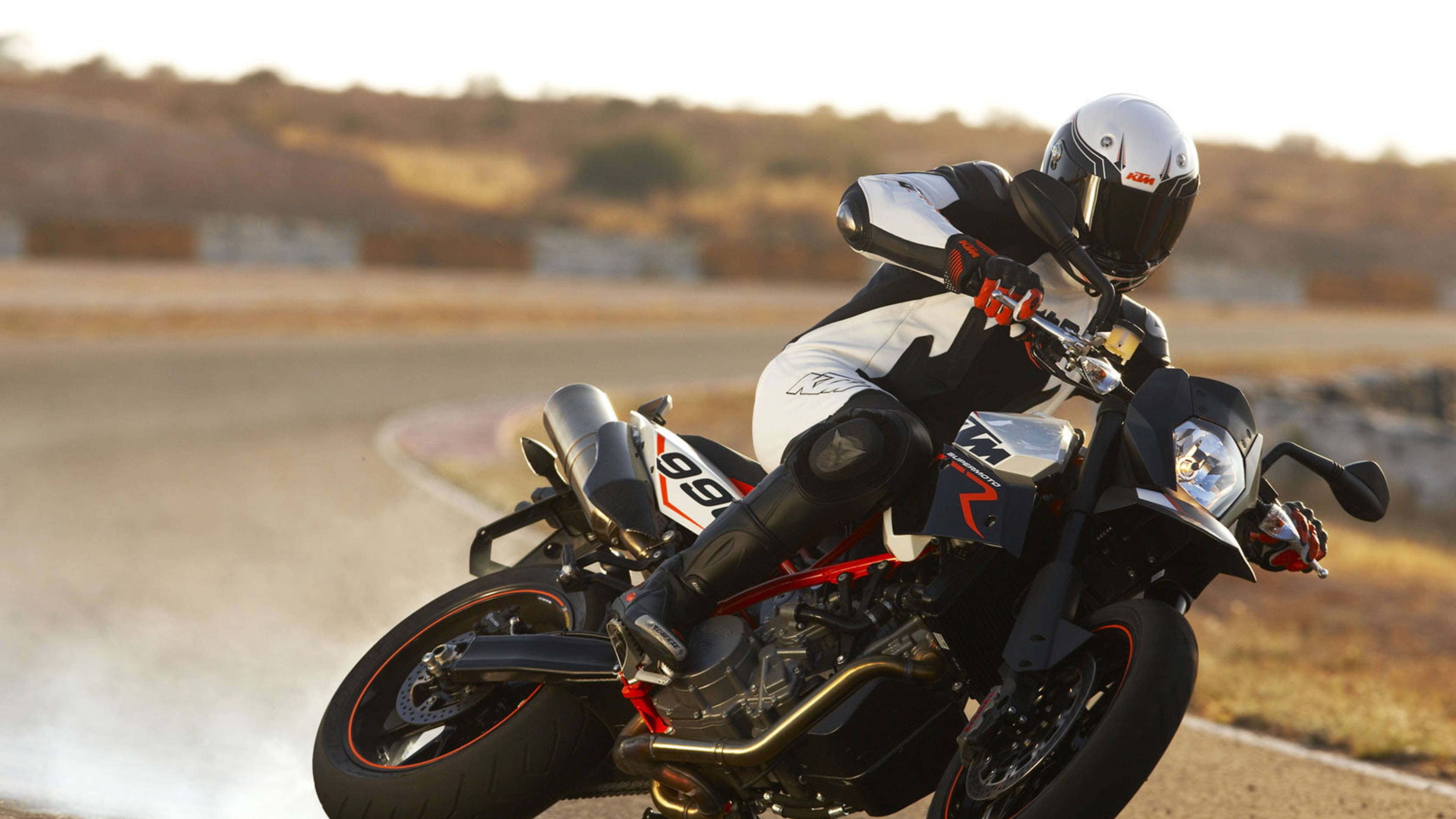 ktm rc 200 桌布 壁紙 — 摩托車手在陽光普照的賽道上，騎著黑紅色跑車傾斜入一個急彎，揚起灰塵。