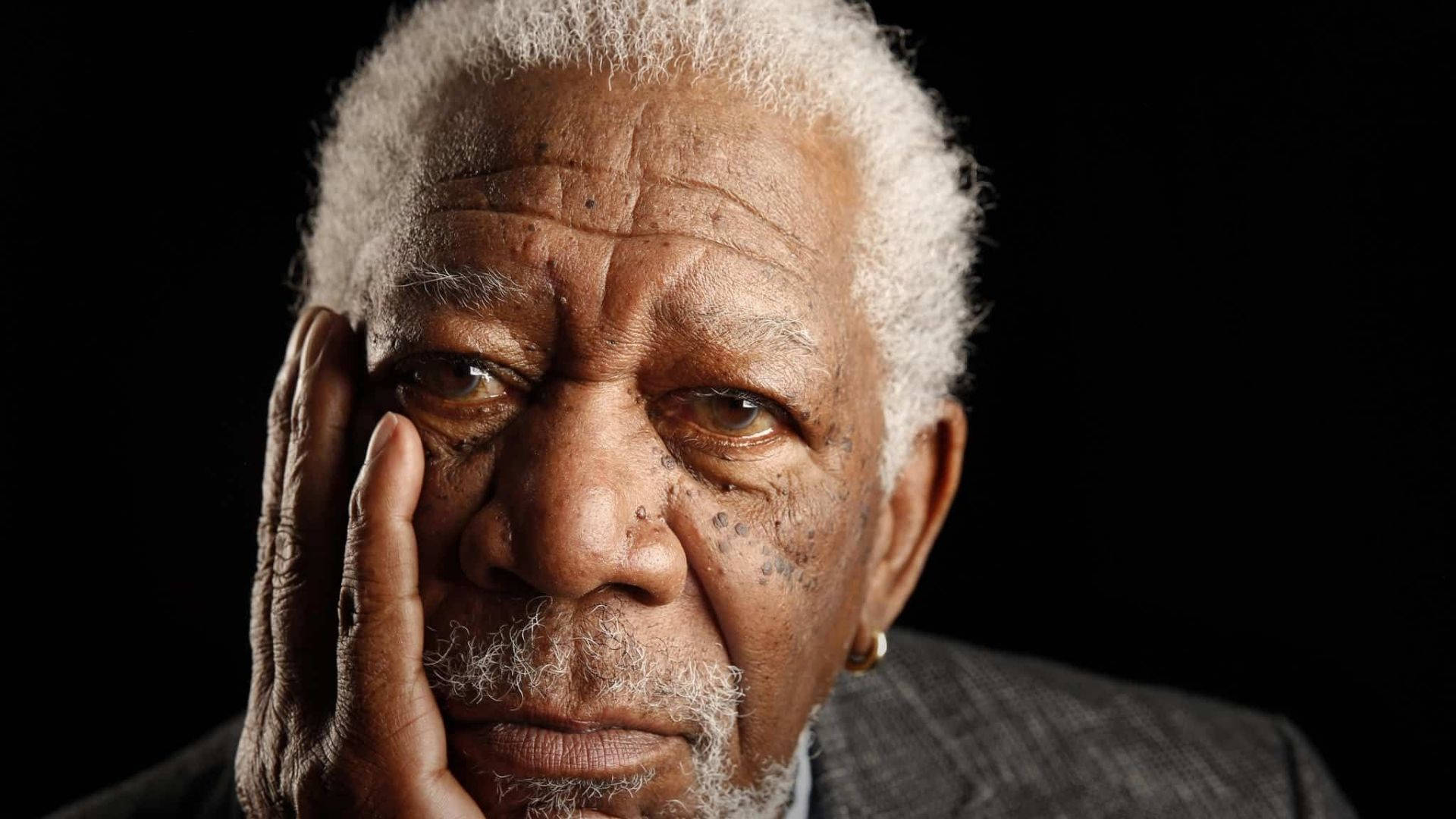 Morgan Freeman 桌布 壁紙 — 摩根費曼的頭像特寫，手托腮，背景為黑色。