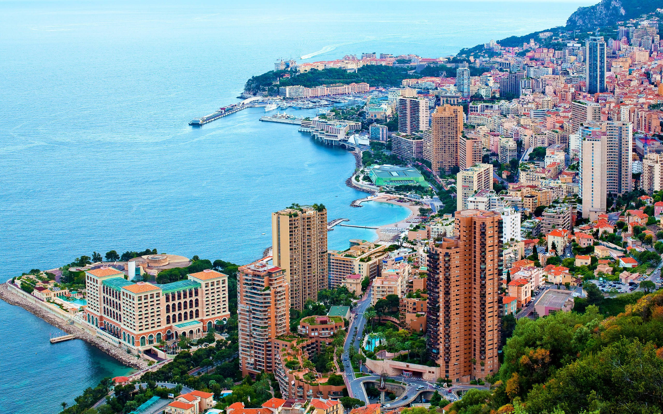 Monaco 桌布 壁紙 — 摩納哥密集沿海城市景觀的鳥瞰圖，豪華酒店和遊艇碼頭坐落在碧綠海水和綠色山丘之間。