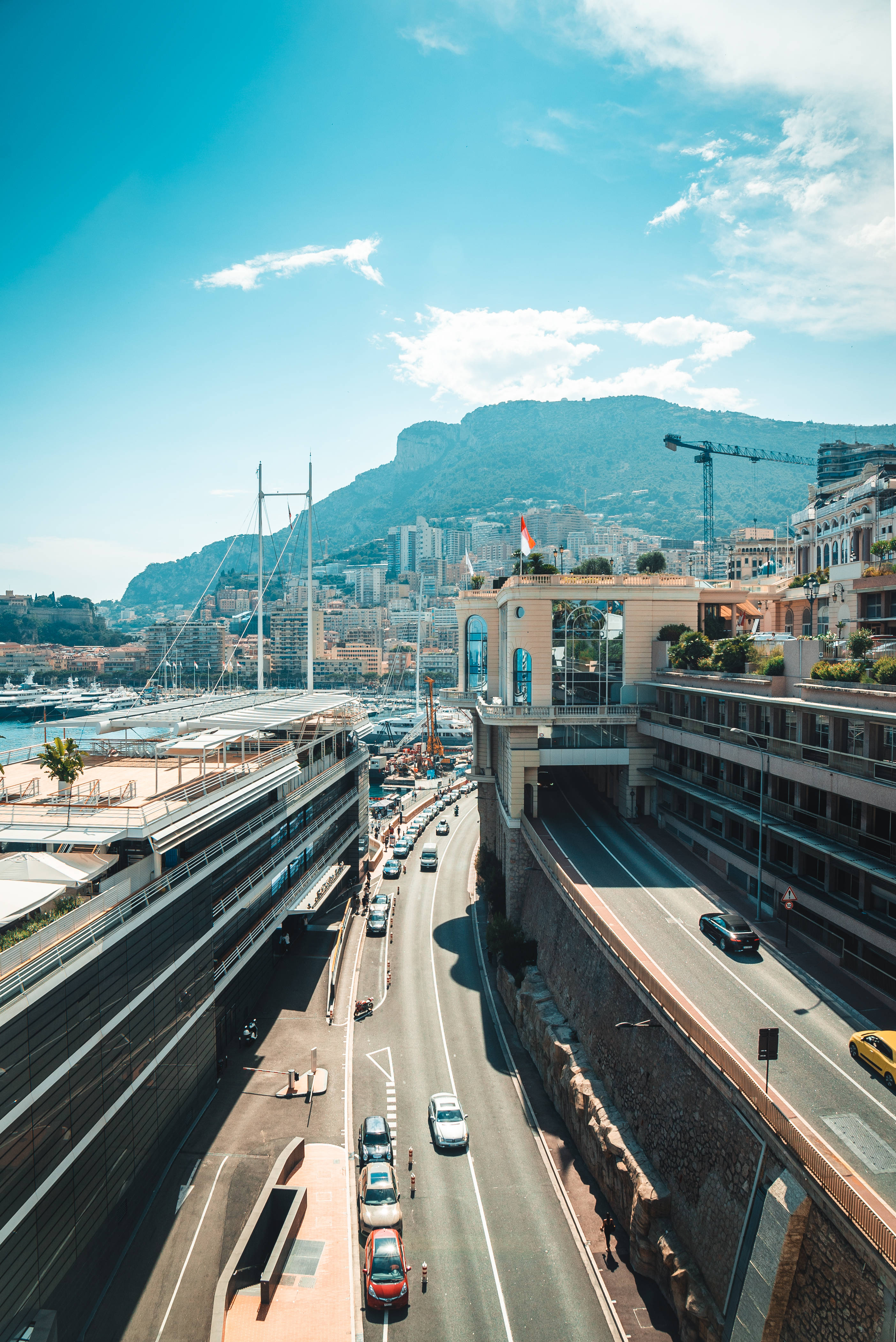 Monaco 桌布 壁紙 — 摩納哥海岸高速公路在陽光照耀下的鳥瞰圖，蜿蜒經過豪華酒店和遊艇碼頭，背景是山巒。
