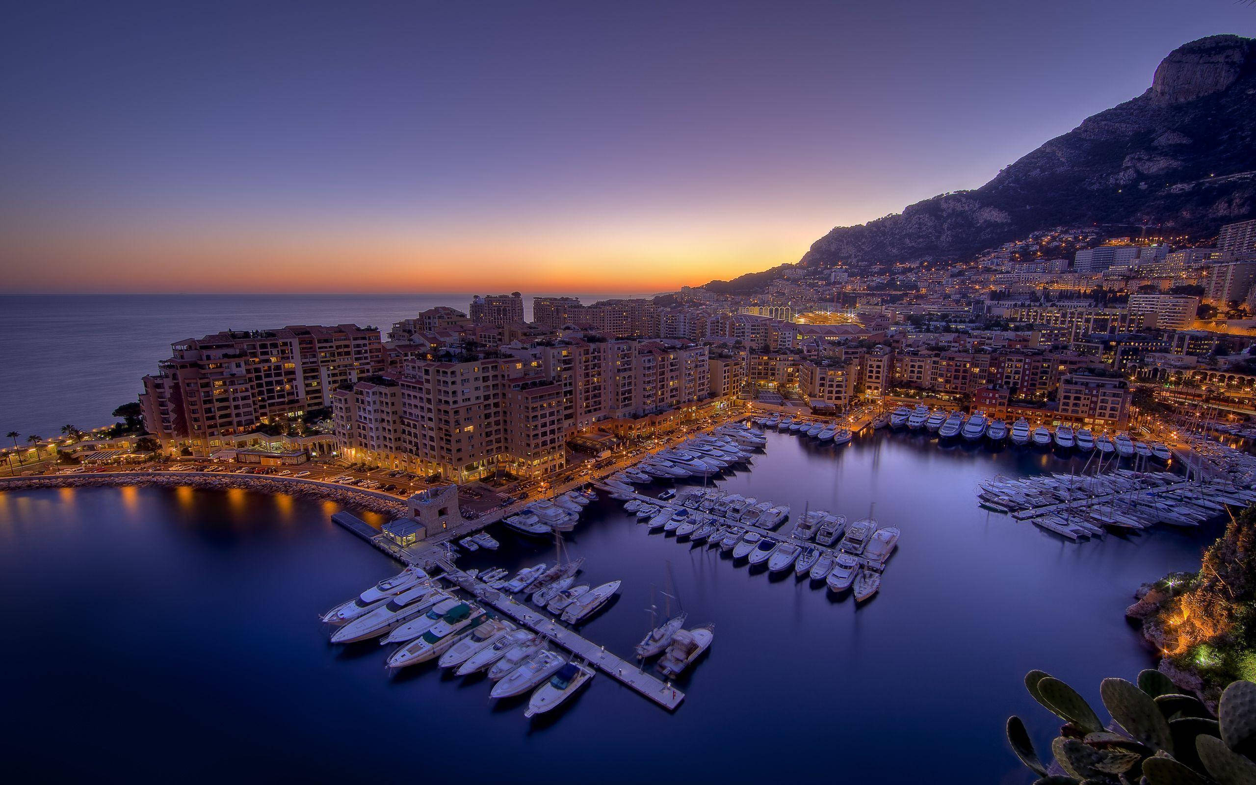Lebanon 桌布 壁紙 — 摩納哥港口的壯麗黃昏景色，停泊著豪華遊艇，城市燈光閃爍，地中海上方呈現鮮豔的橙色地平線。