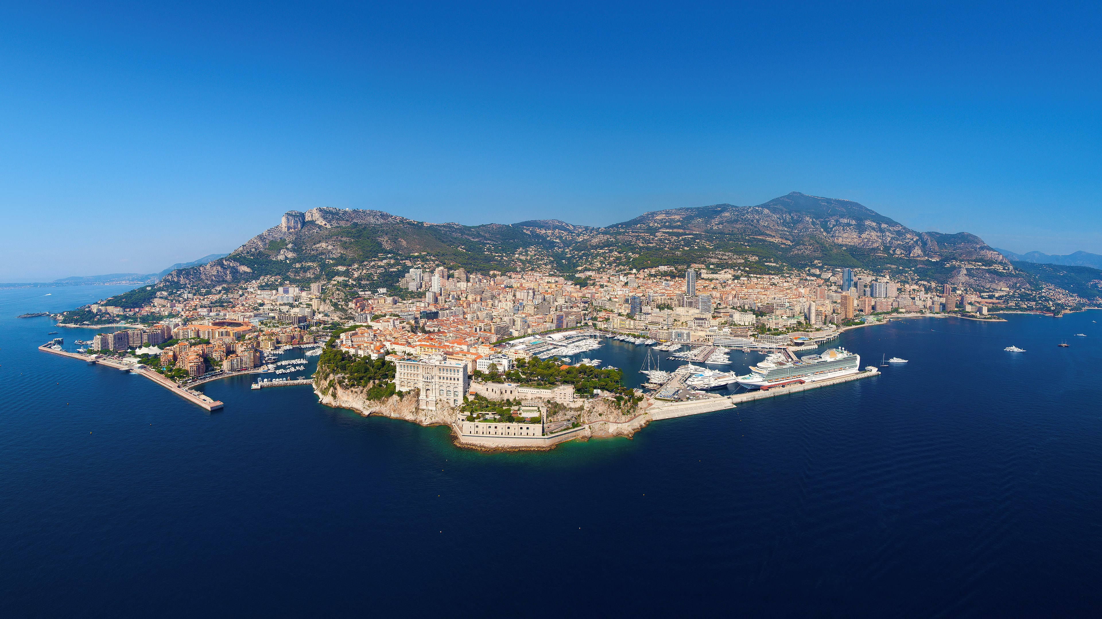 Monaco 桌布 壁紙 — 摩納哥的鳥瞰圖，坐落於深藍色海洋與陽光普照的山脈之間，天空晴朗。