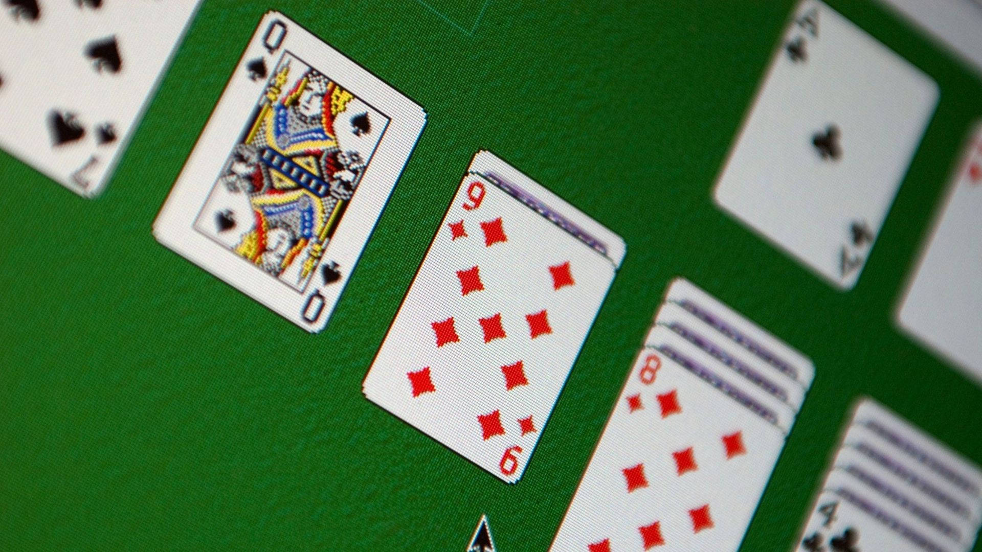 Solitaire 桌布 壁紙 — 撲克牌散落在綠色絨面桌面上的特寫，焦點清晰對準黑桃皇后和方塊九。