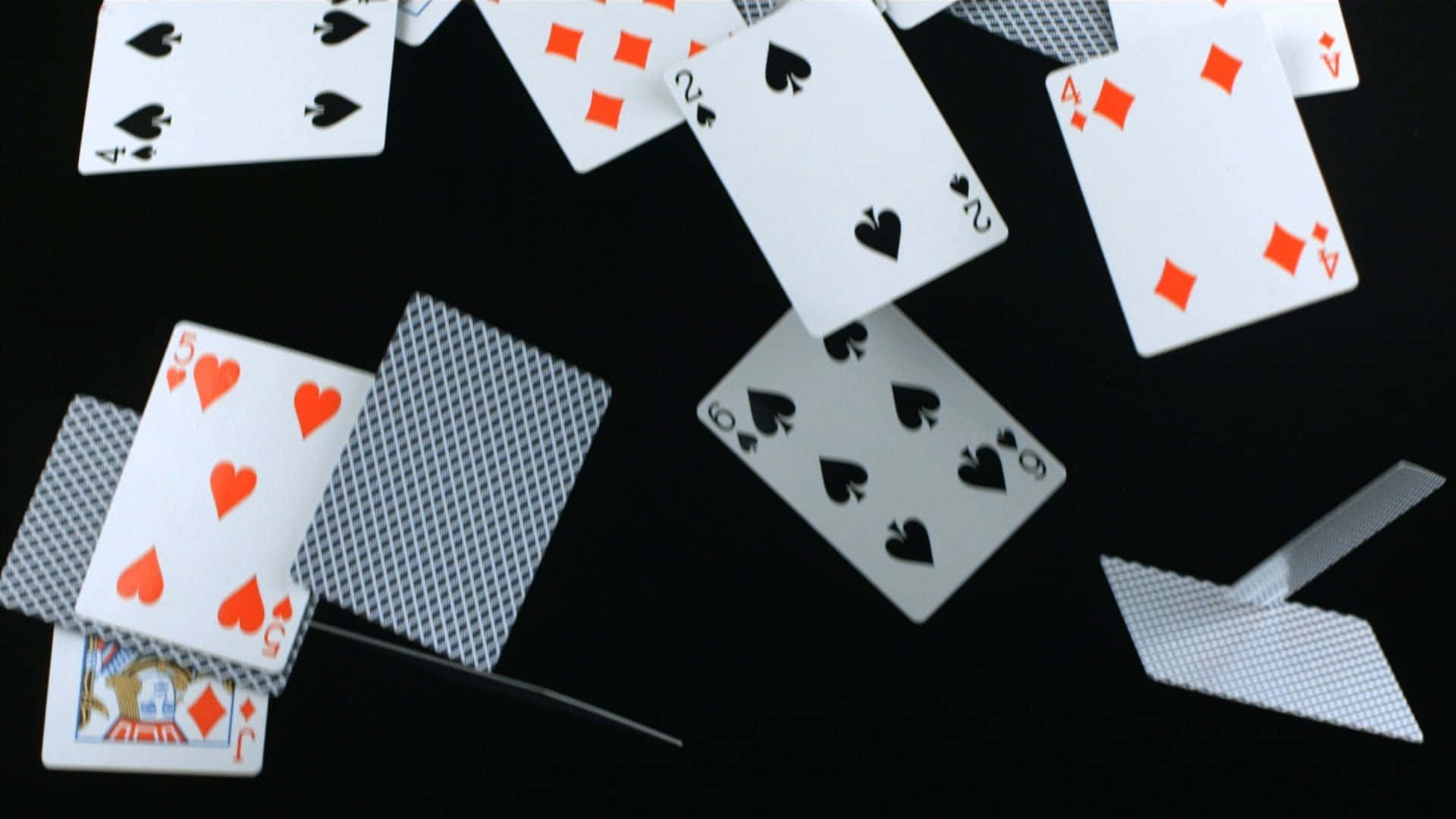 Card Games 桌布 壁紙 — 撲克牌散落在黑色表面上，有些牌面向上，有些牌面向下。