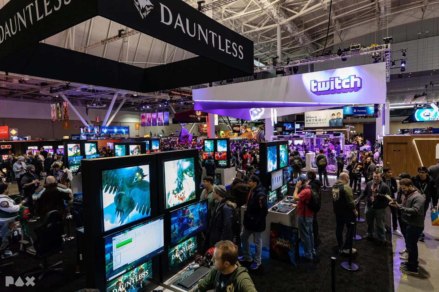 Gaming Conventions 桌布 壁紙 — 擁擠的遊戲展覽廳，玩家在Dauntless和Twitch展位前，上方明亮的燈光照射。