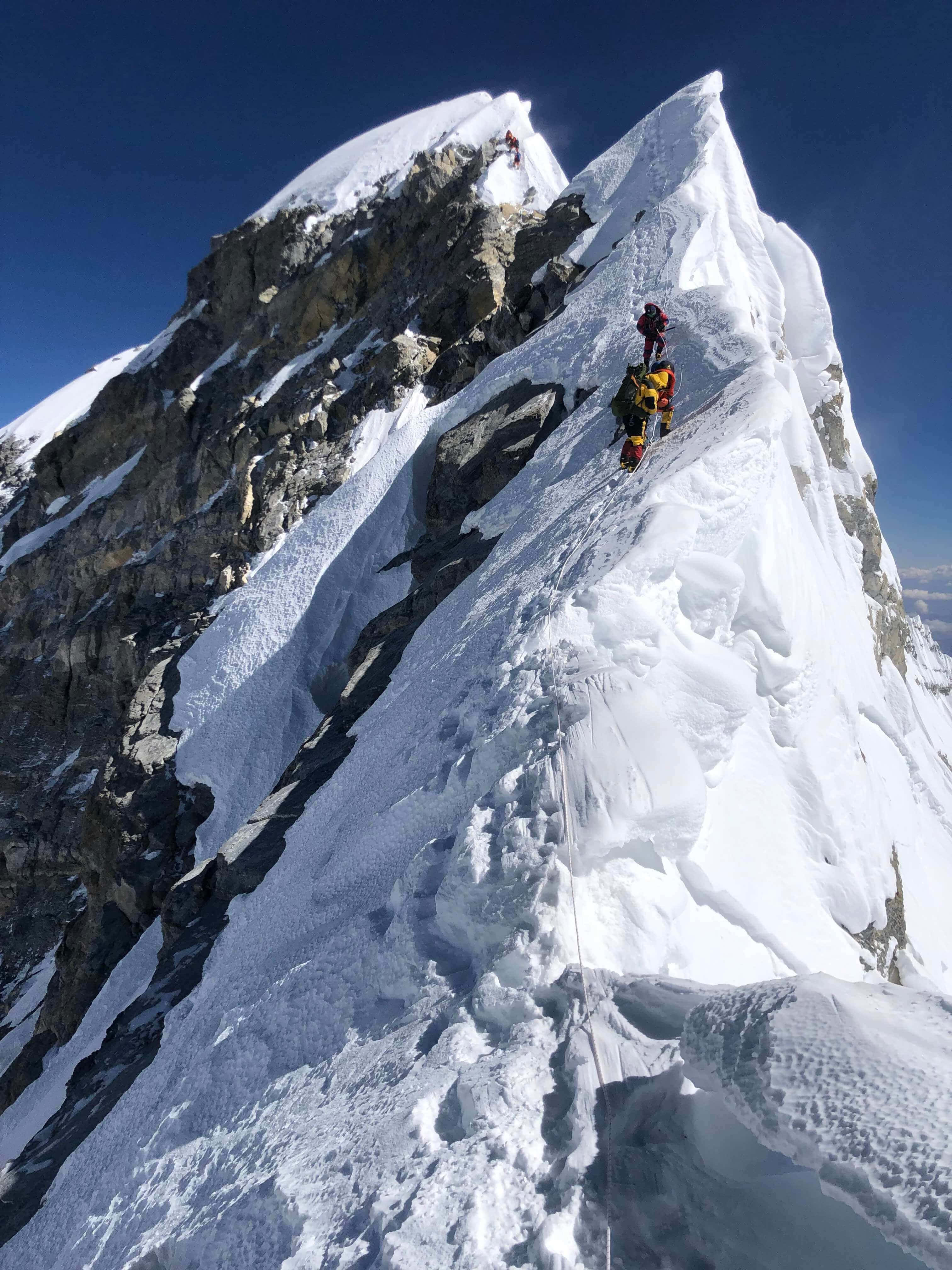 Mount Everest 桌布 壁紙 — 攀岩者在晴朗的藍天下攀登陡峭的積雪山脊，露出岩石表面。