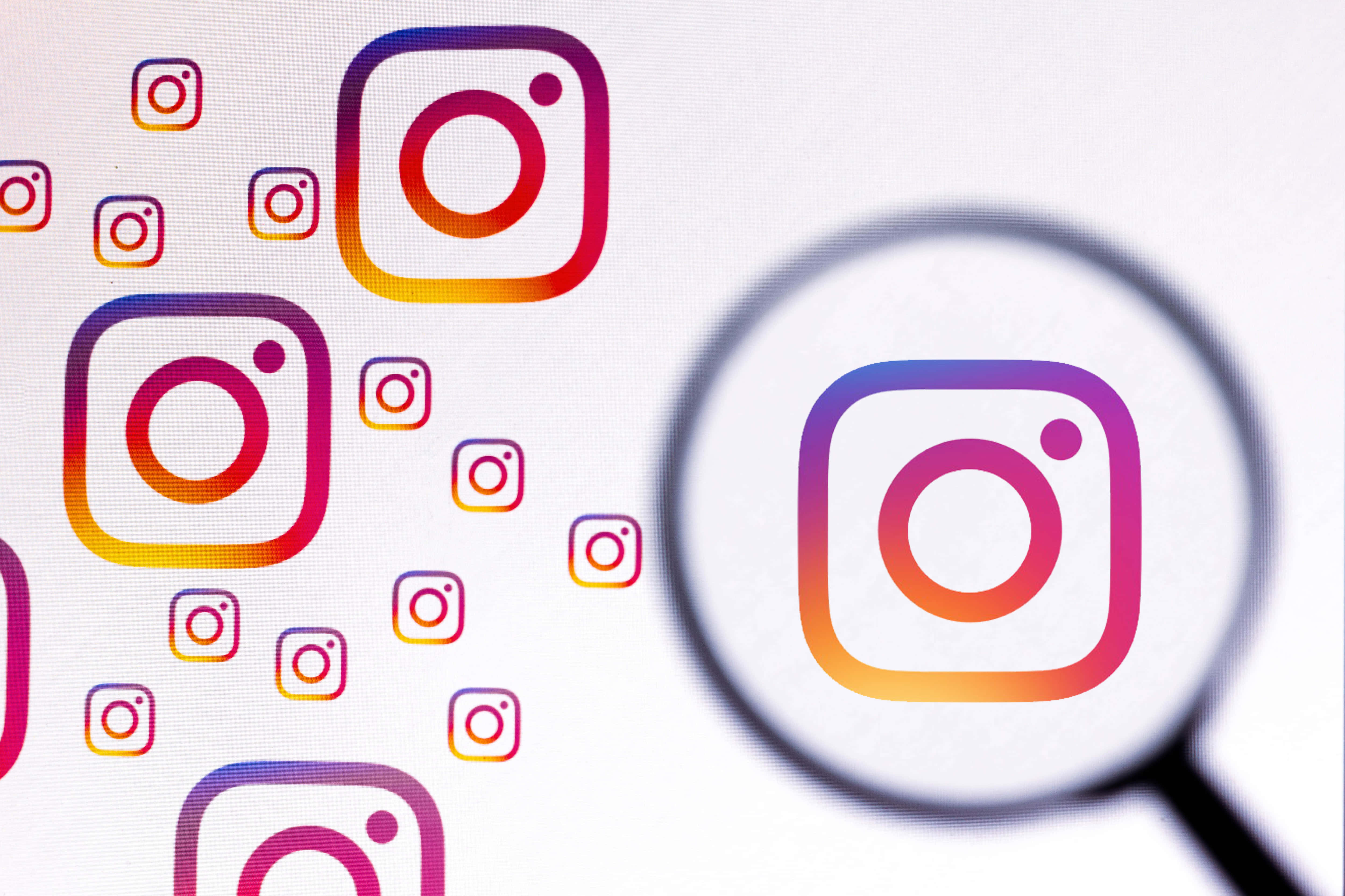 Instagram 桌布 壁紙 — 放大鏡聚焦在白色表面上散落的彩色應用程式圖示中的一個鮮豔的Instagram標誌上。