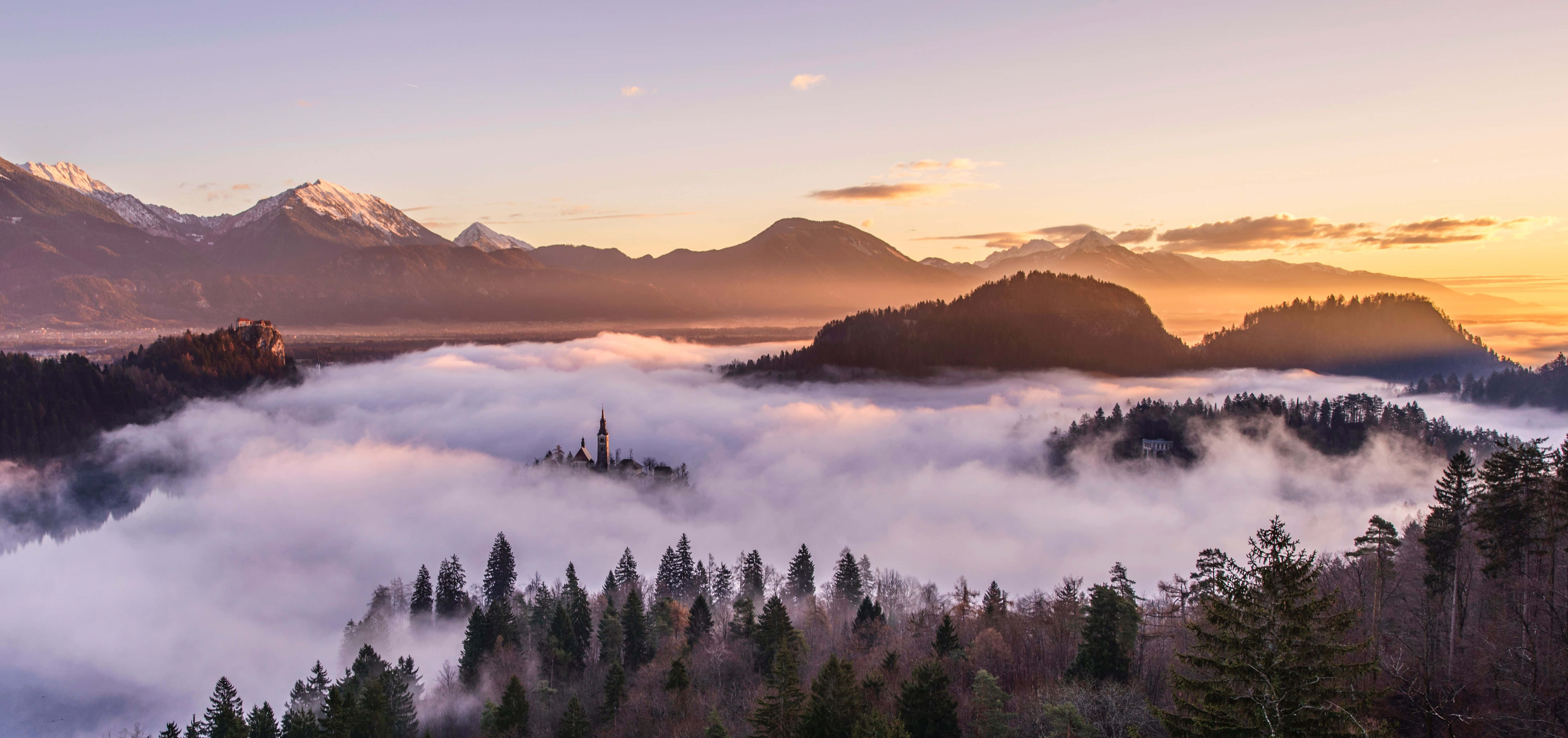 Photography Desktop 桌布 壁紙 — 教堂尖頂聳立於松林間的霧海之上，雪山在日出時閃耀光芒。